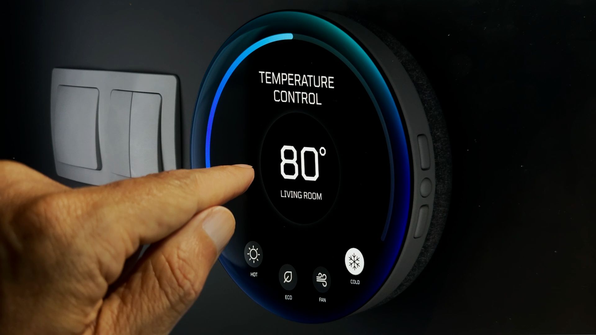 A close up shot of someone's hand as they adjust the temperature on a modern looking thermostat