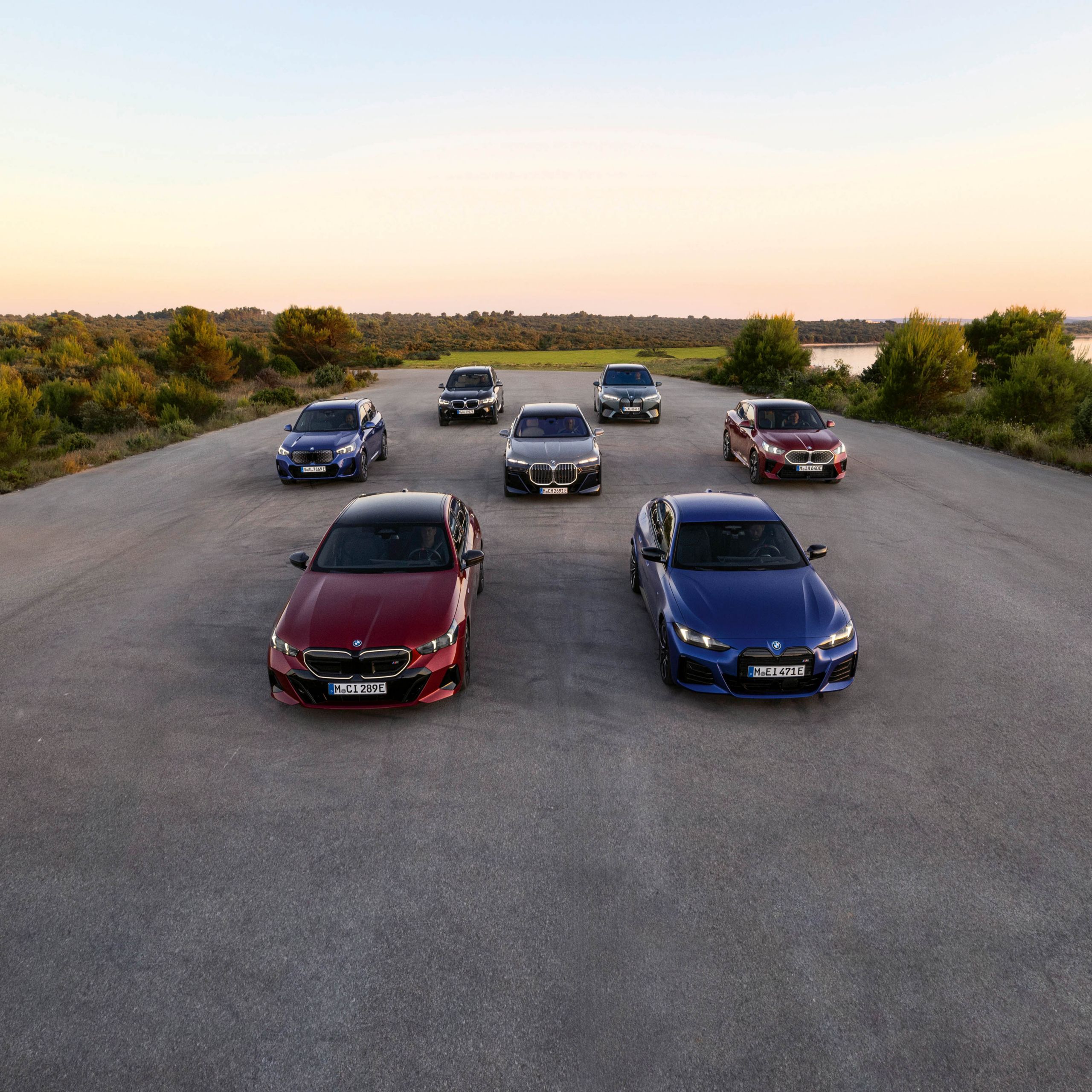 BMW elbilar uppradade på en parkering med natur i bakgrunden.
