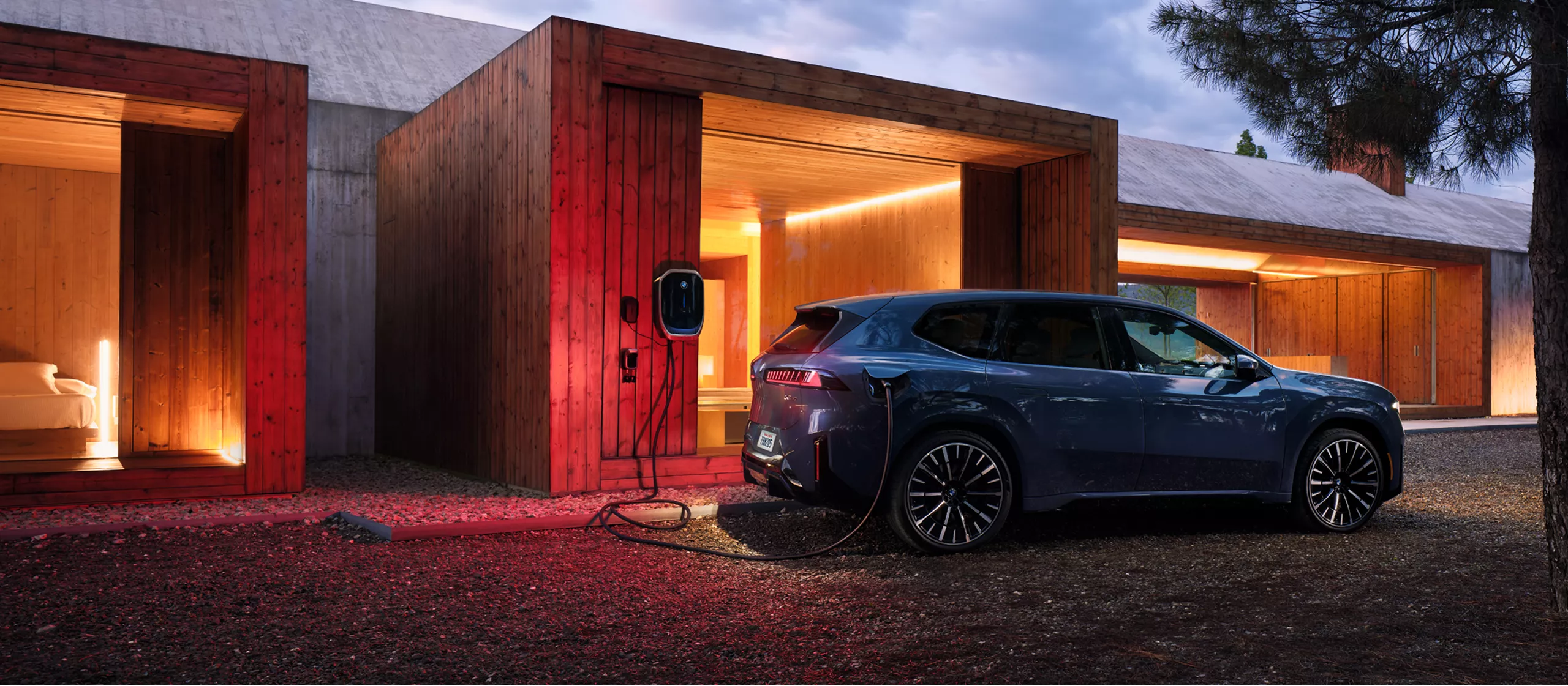 A BMW iX3 is plugged into a BMW Wallbox attached to a modern wooden structure. 