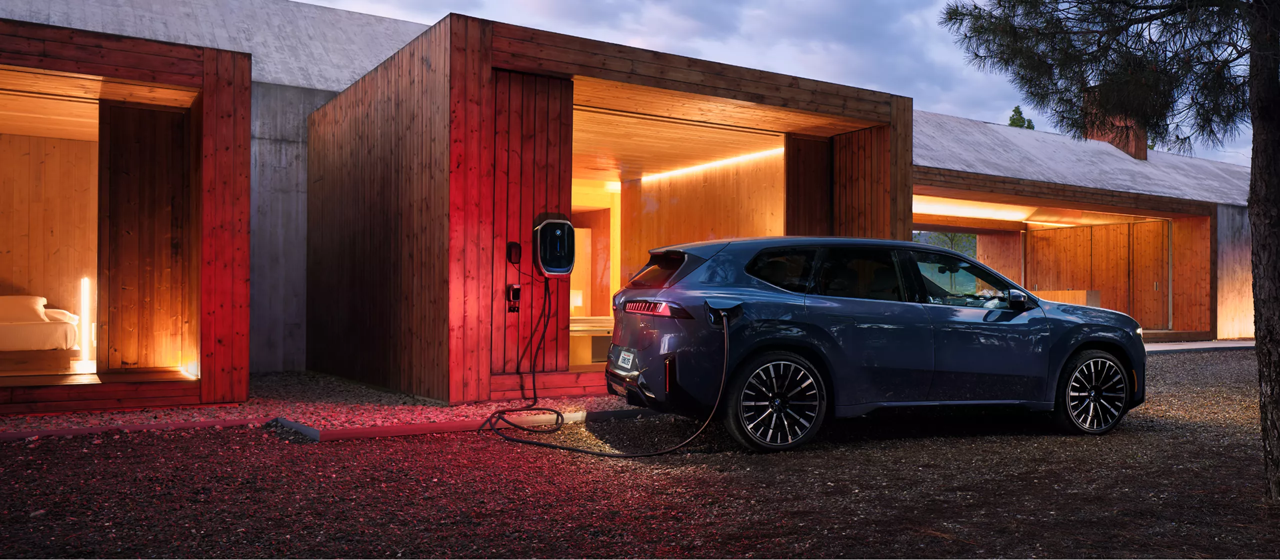 A BMW iX3 is plugged into a BMW Wallbox attached to a modern wooden structure. 