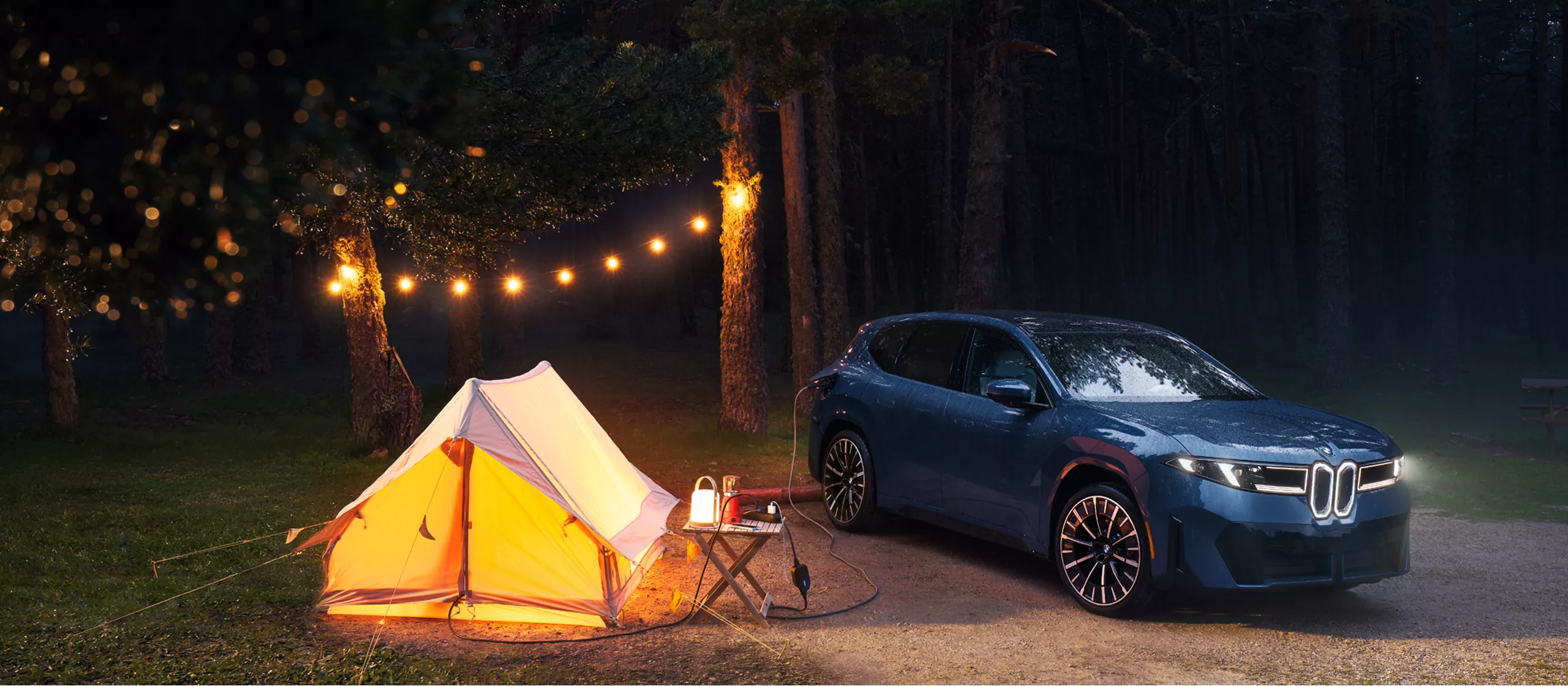 A BMW iX3 is parked at a campground while its charging cable leading into the tent to provide power 