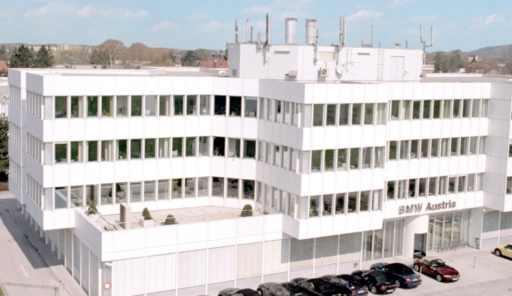 Ansicht der Vorderseite des BMW Group Standort Salzburg Campus Süd. Davor parken verschiedene Fahrzeuge.