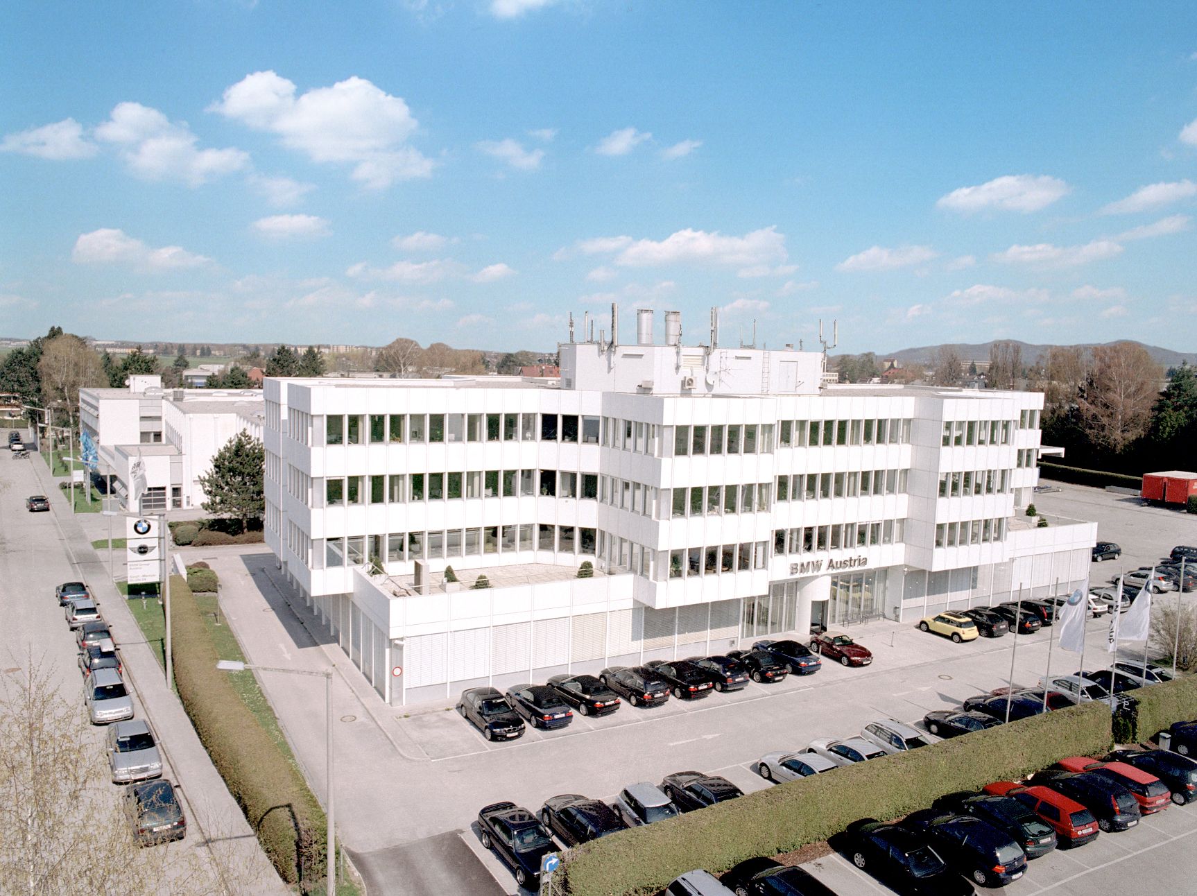 Ansicht der Vorderseite des BMW Group Standort Salzburg Campus Süd. Davor parken verschiedene Fahrzeuge.