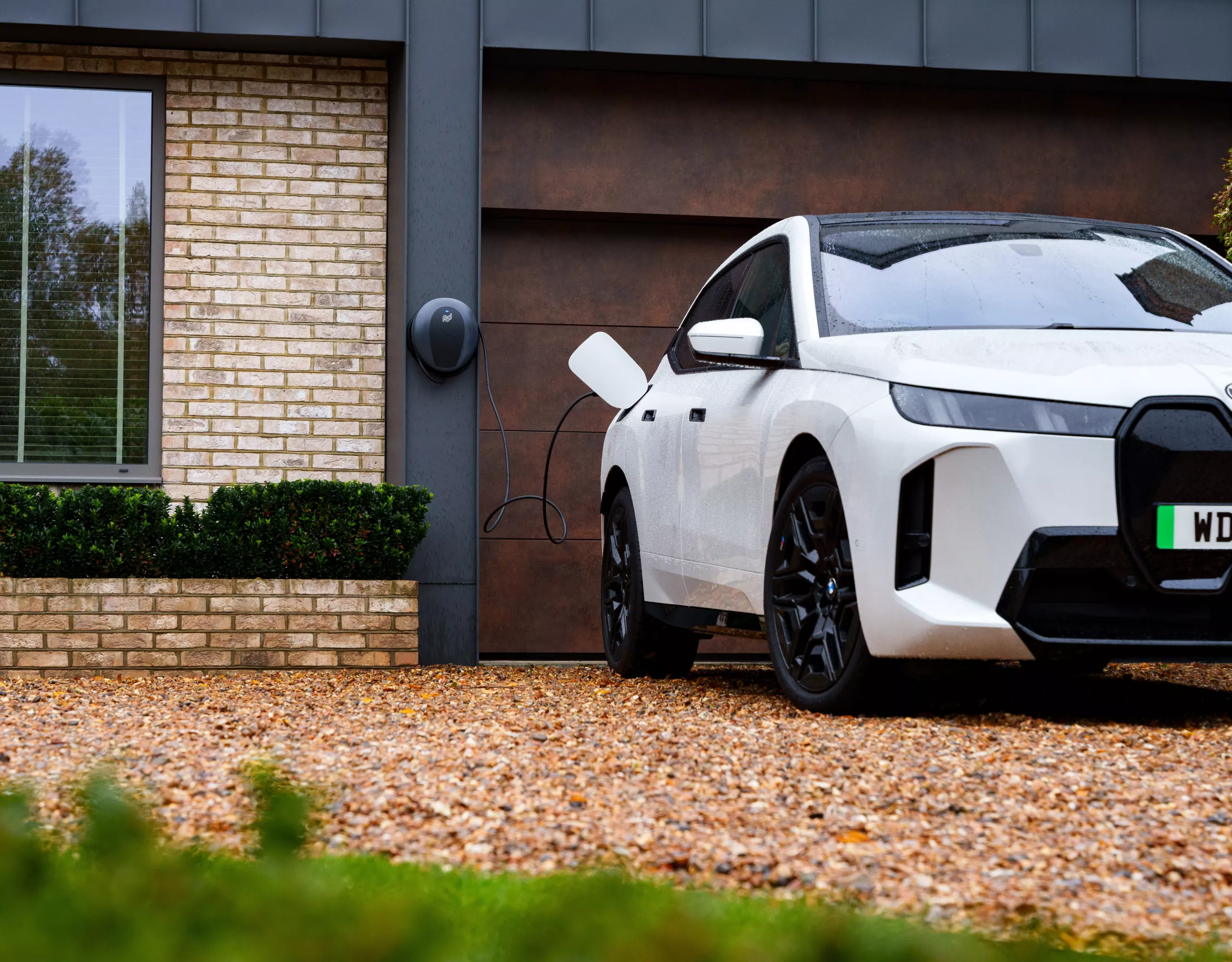 A BMW is being charged at a Wallbox at home with plants in the background 