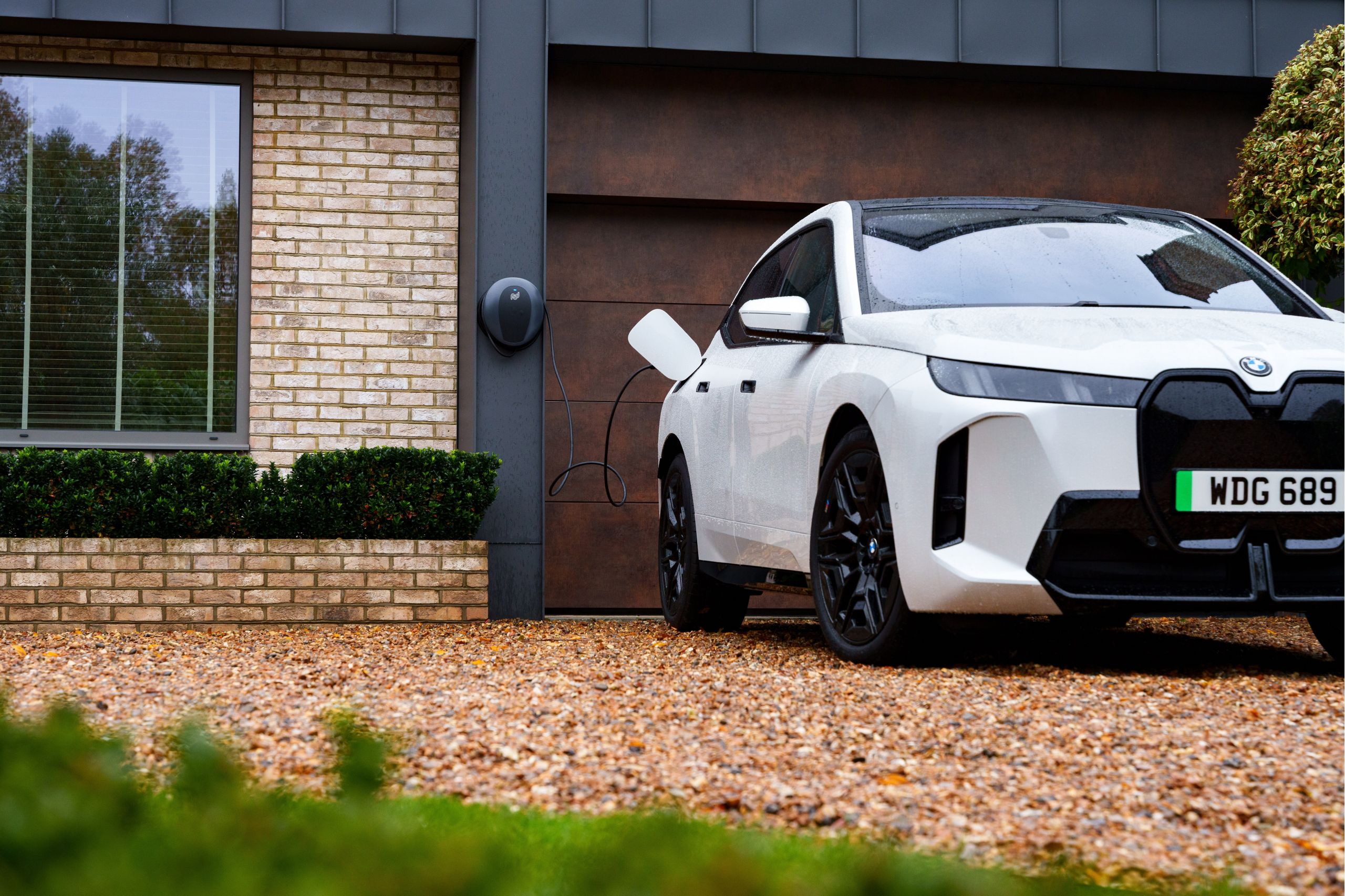 A BMW is being charged at a Wallbox at home with plants in the background 