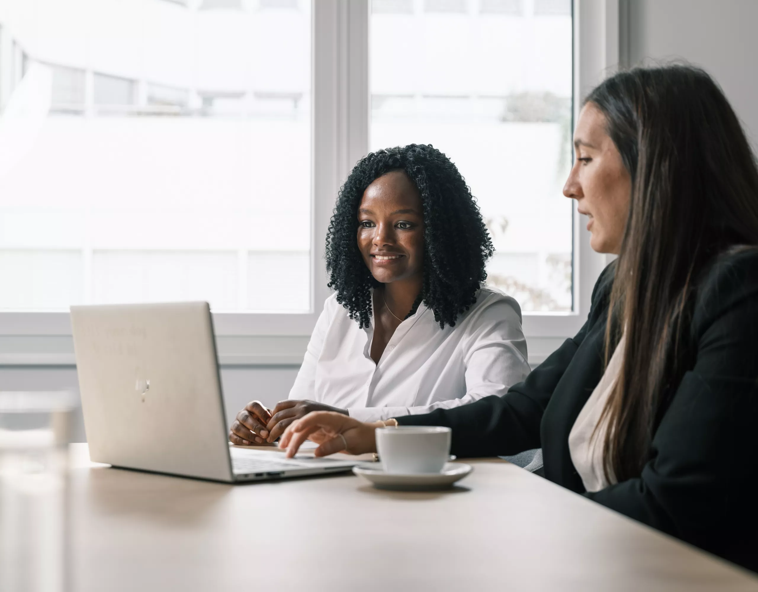 Zwei Mitarbeiterinnen der BMW Group arbeiten zusammen an einem silbernen HP-Laptop.