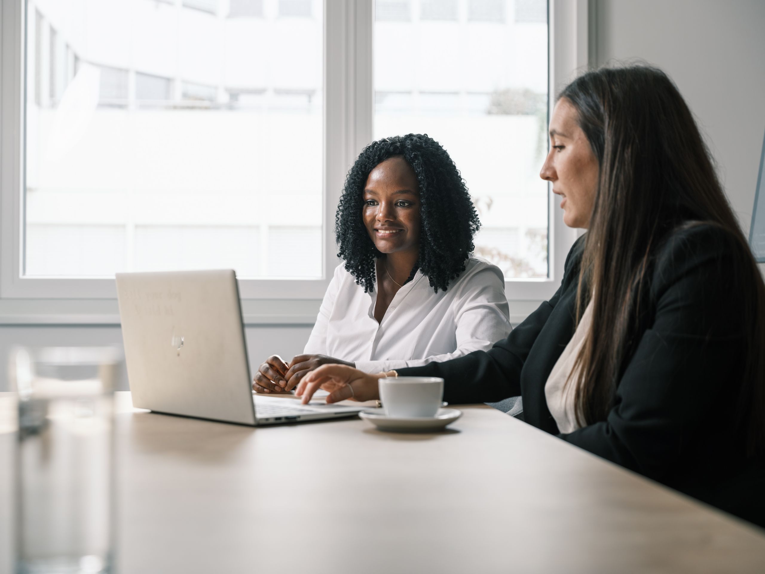 Zwei Mitarbeiterinnen der BMW Group arbeiten zusammen an einem silbernen HP-Laptop.