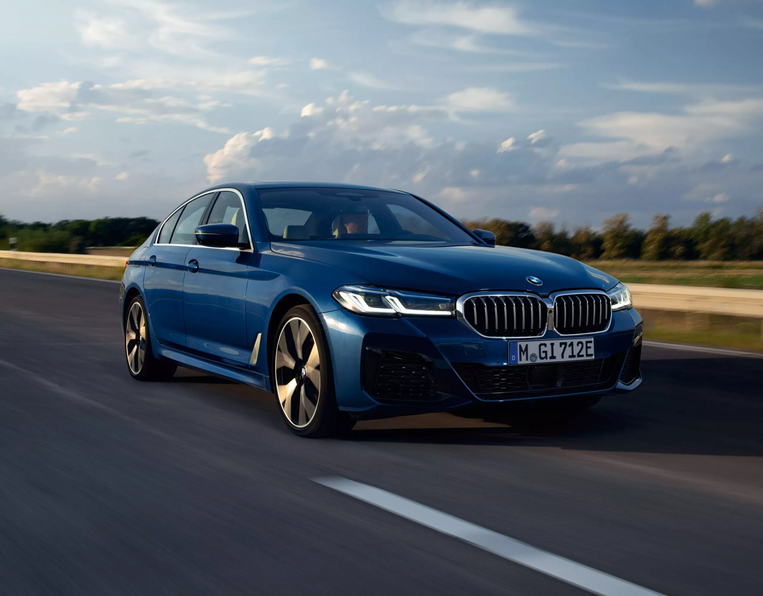 Blauer BMW fährt auf einer Straße durch eine Landschaft.