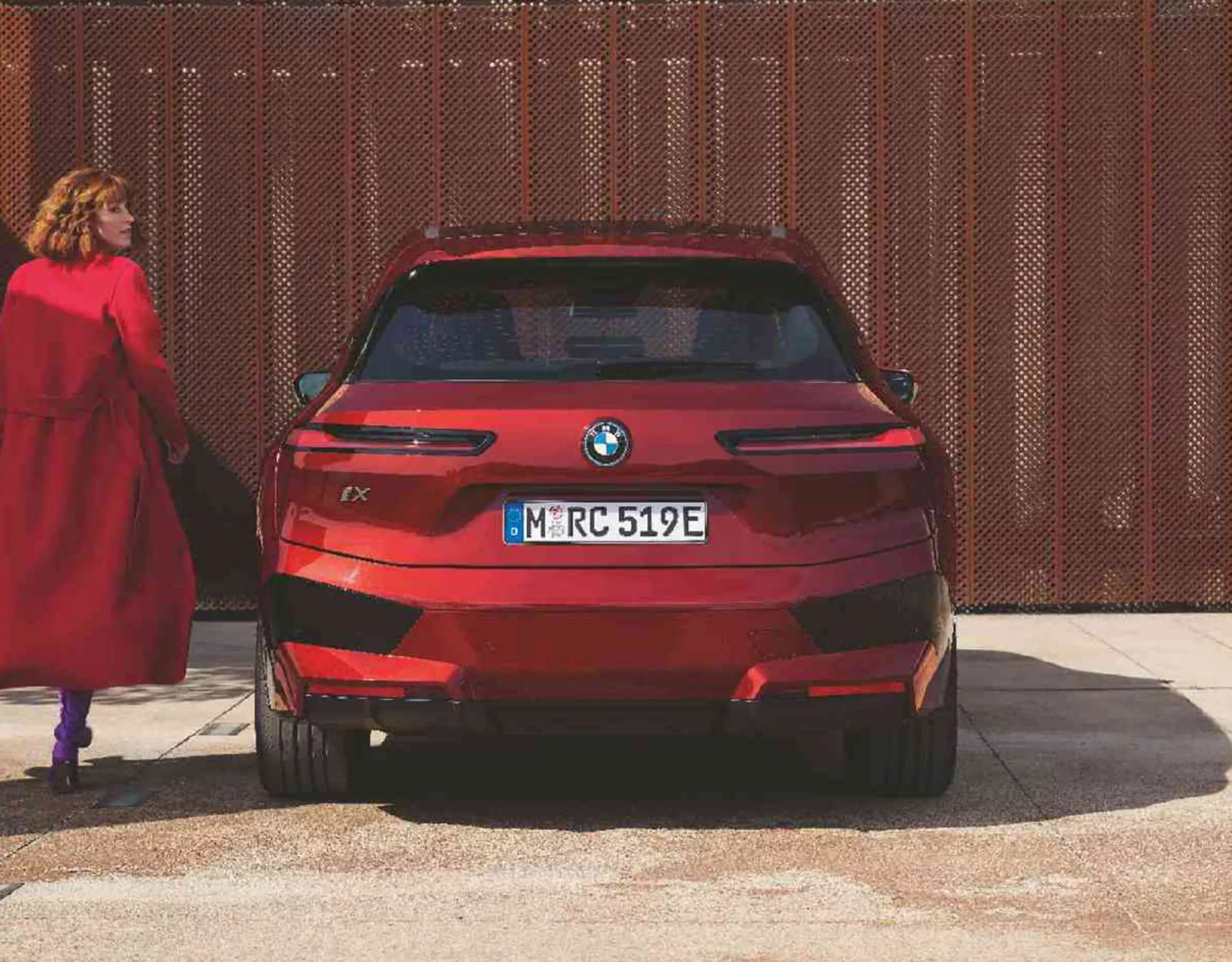 Un groupe de personnes avec des sacs à dos et des casques s’avance vers un mur d’escalade. Une BMW est garée à côté