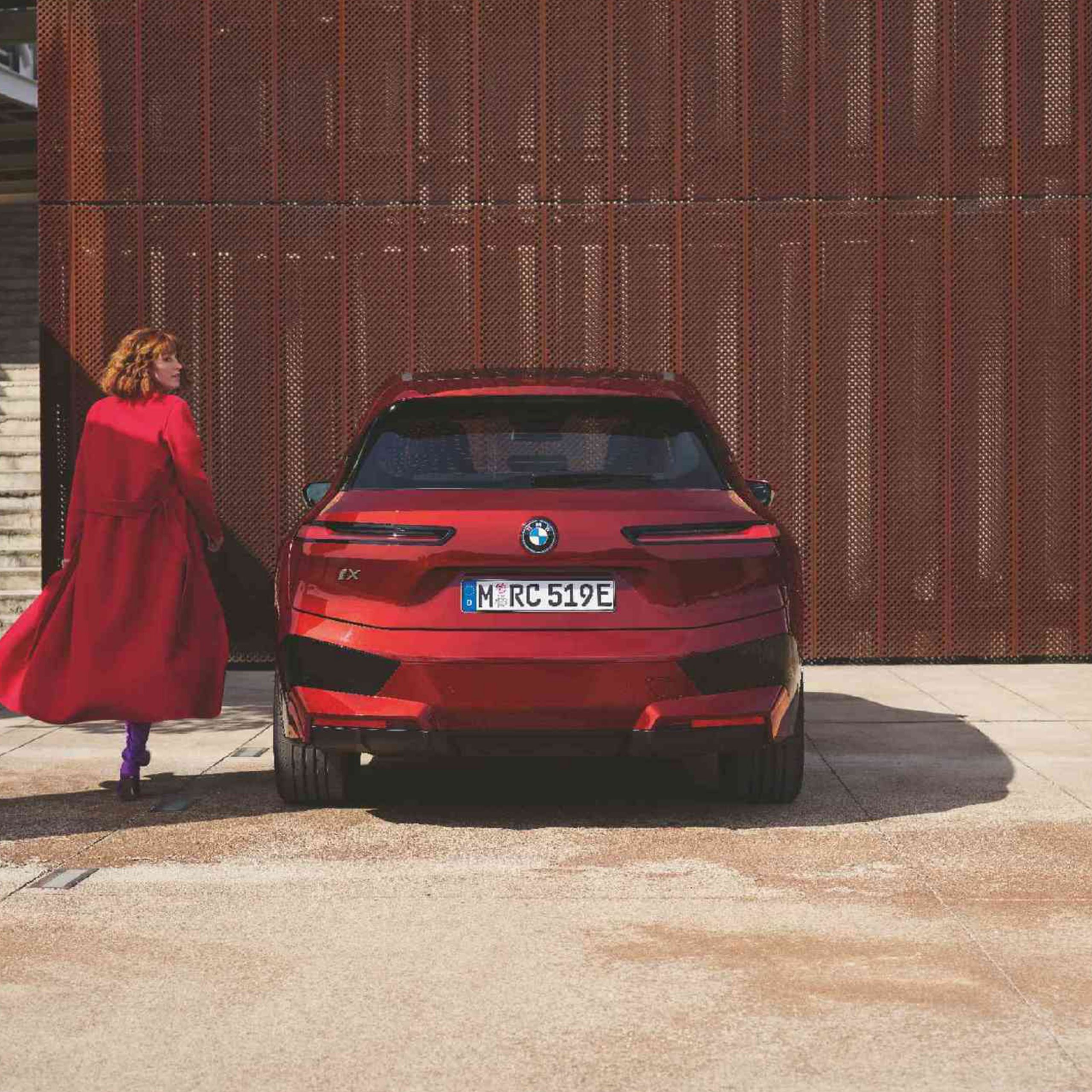 A group of people with backpacks and helmets approach a climbing wall. Next to them is a parked BMW