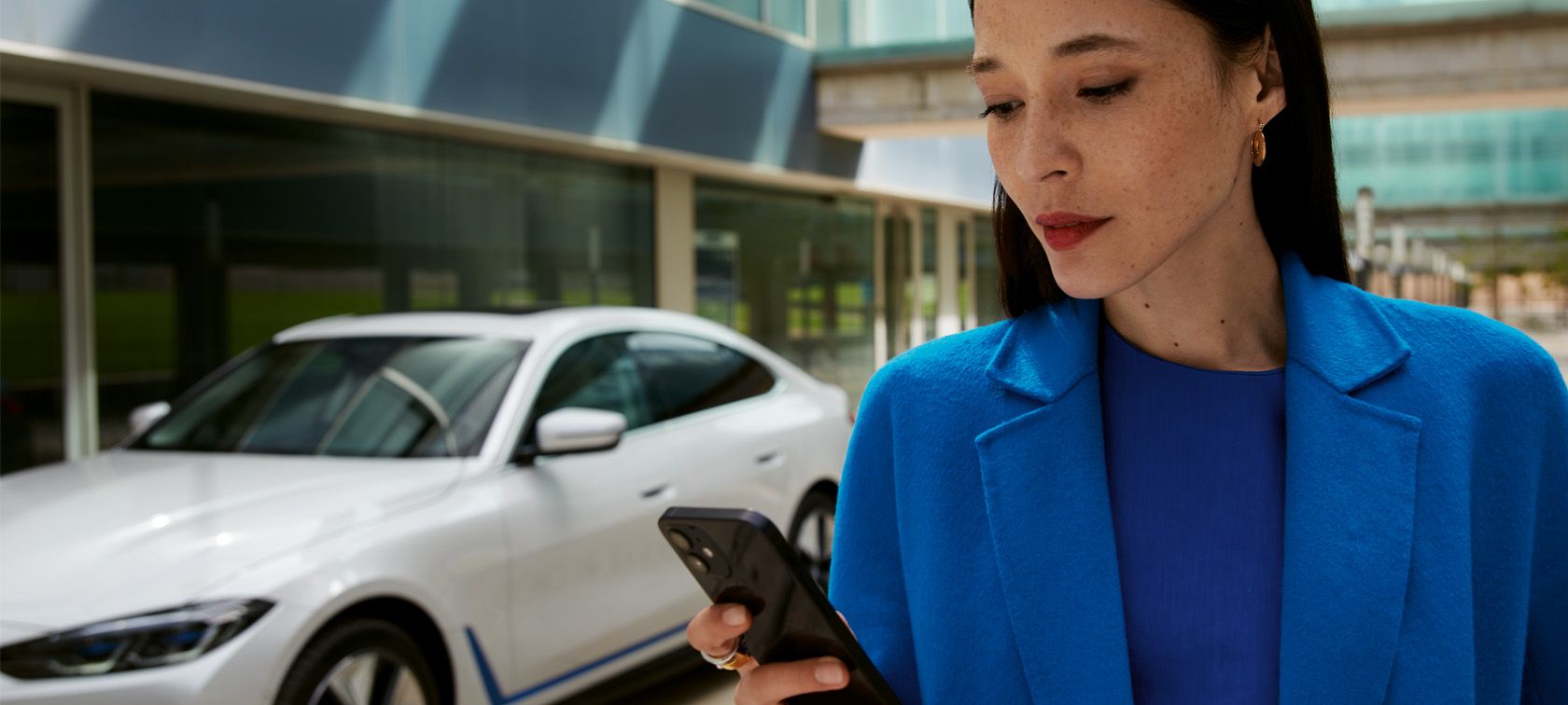 Femme devant la BWW i4 qui utilise son smartphone.