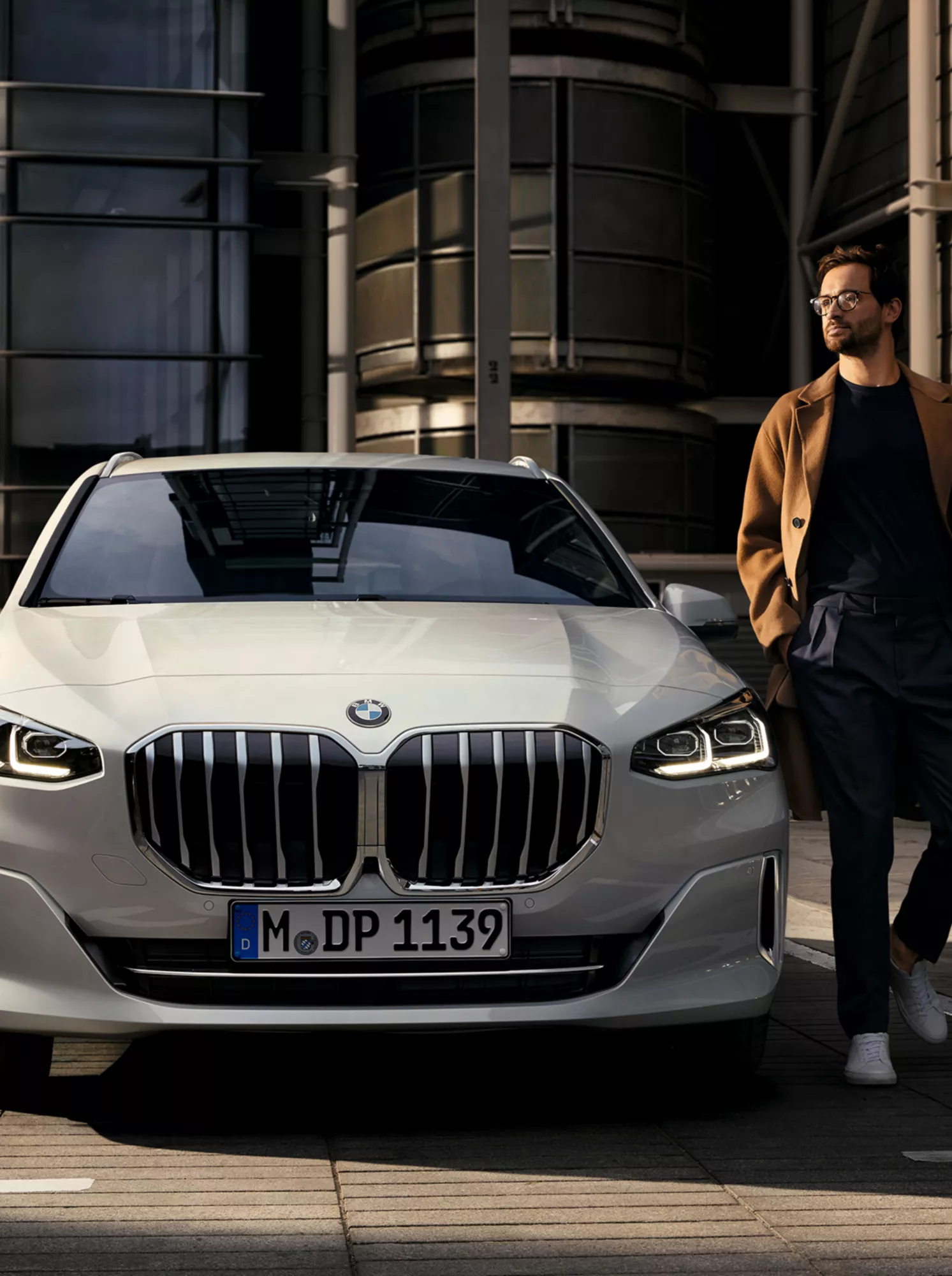 近代的なアパートの前に駐車しているBMW 2シリーズ アクティブ ツアラーとその横を歩いている人物 