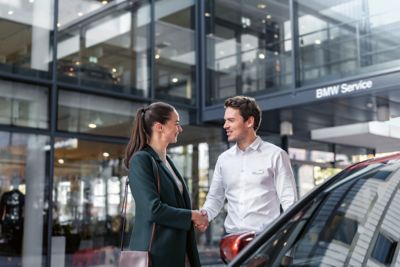 Mann und Frau geben sich die Hand vor einem Auto in einem BMW Service Betrieb