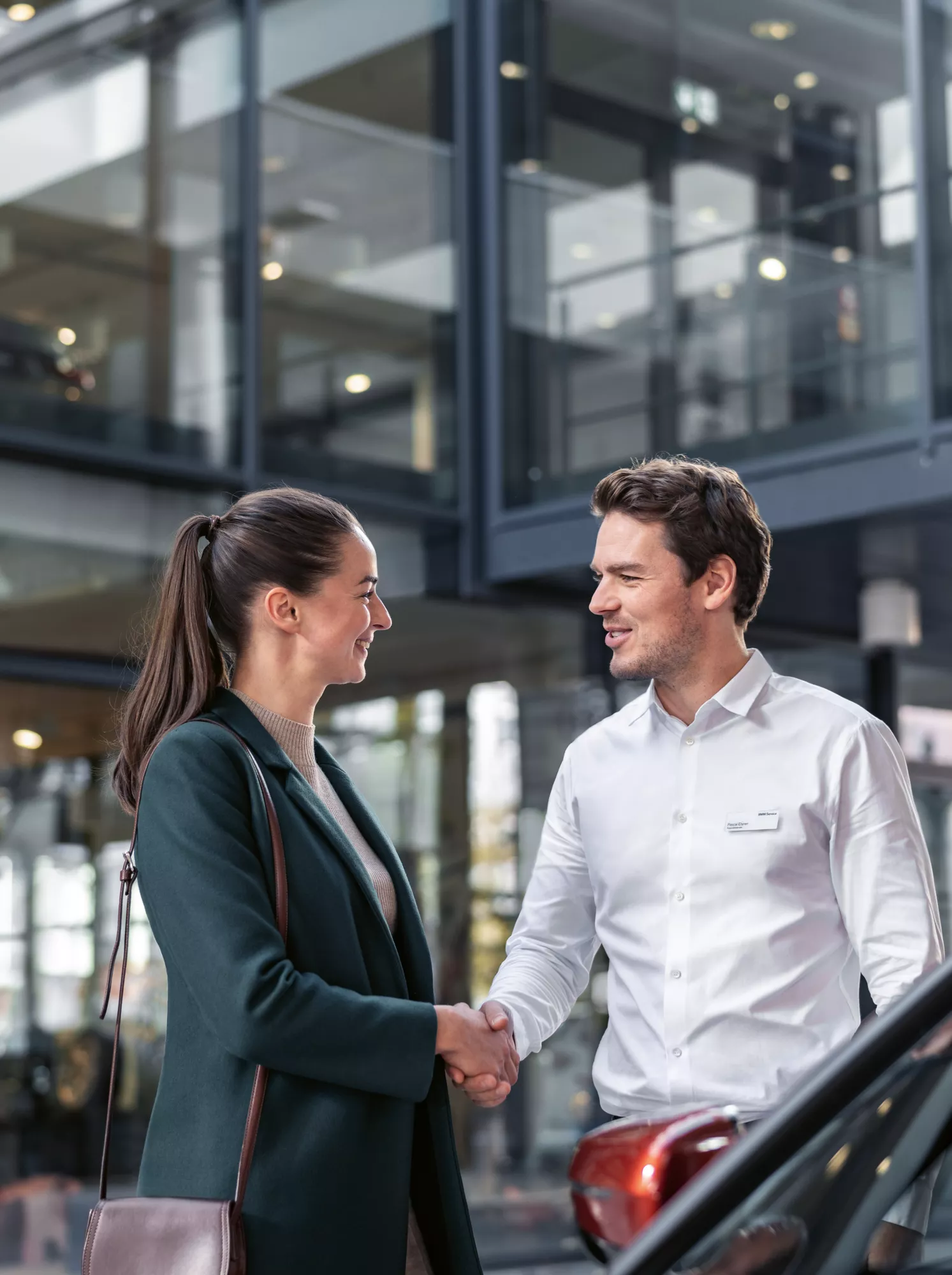 Un homme et une femme se serrent la main devant une voiture dans une entreprise de service BMW.