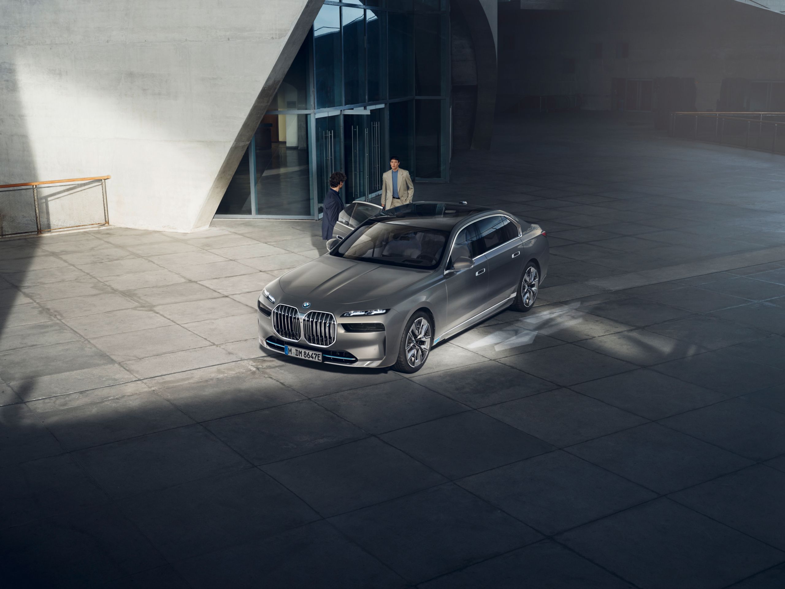 Vista de cima de duas pessoas junto a um veículo diplomático BMW em frente a um edifício