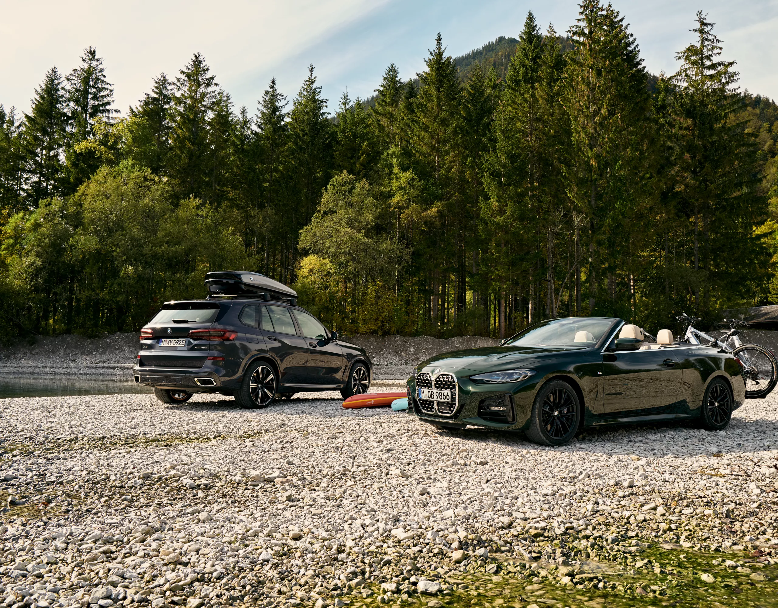  Dois BMW equipados com suporte para bicicletas e caixa de tejadilho estacionados lado a lado ao pé de um lago.