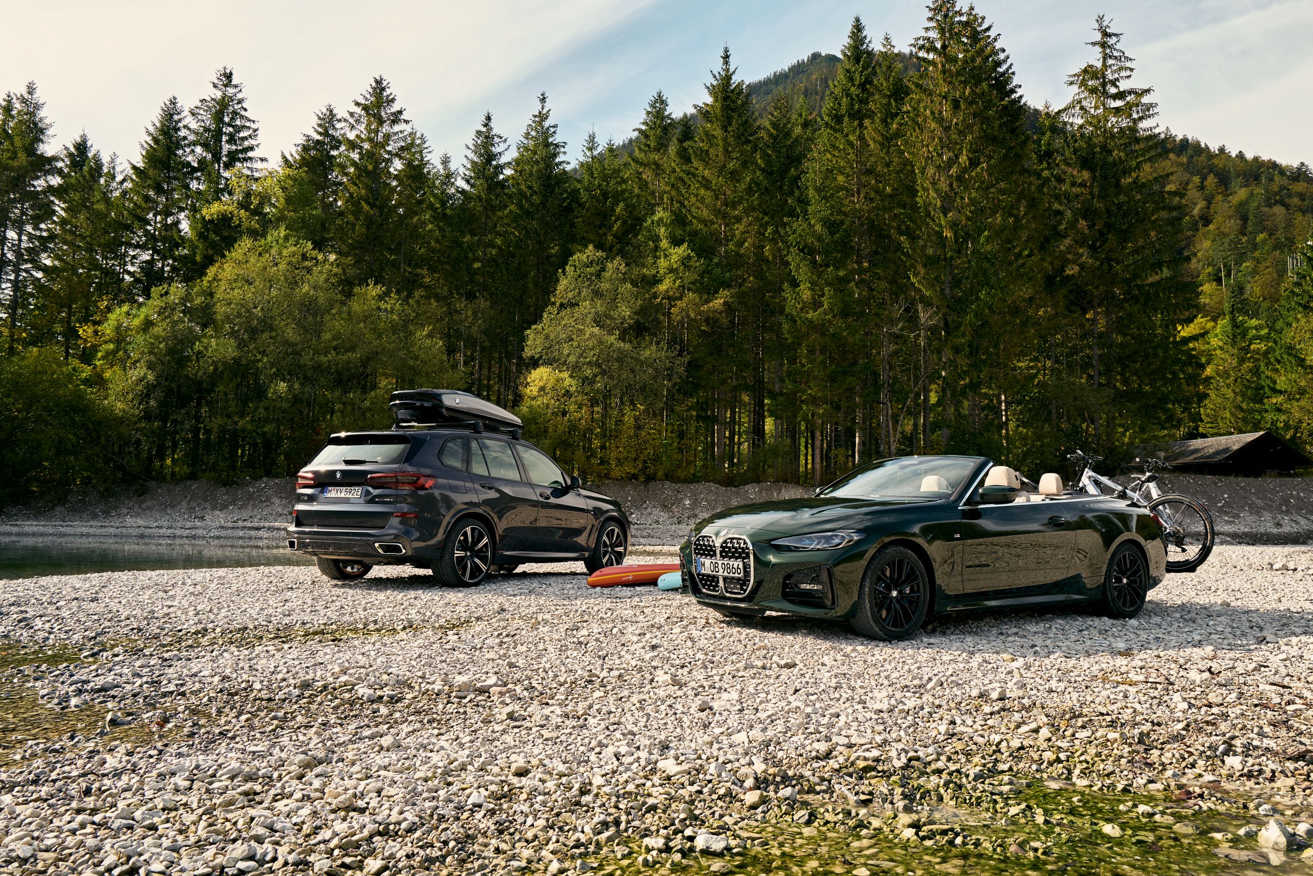  Dois BMW equipados com suporte para bicicletas e caixa de tejadilho estacionados lado a lado ao pé de um lago