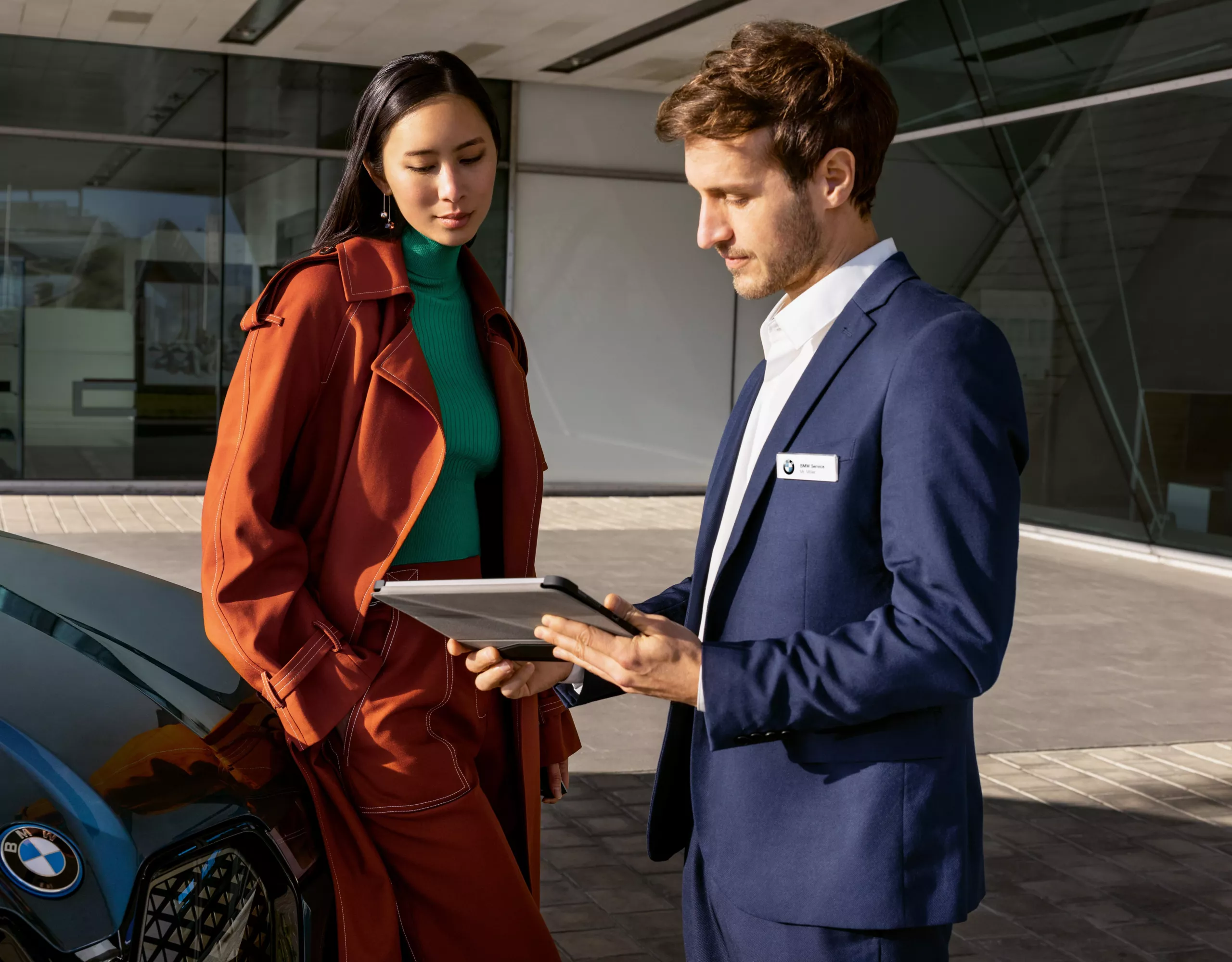 A woman is standing between two fully electric BMW vehicles in front of a building