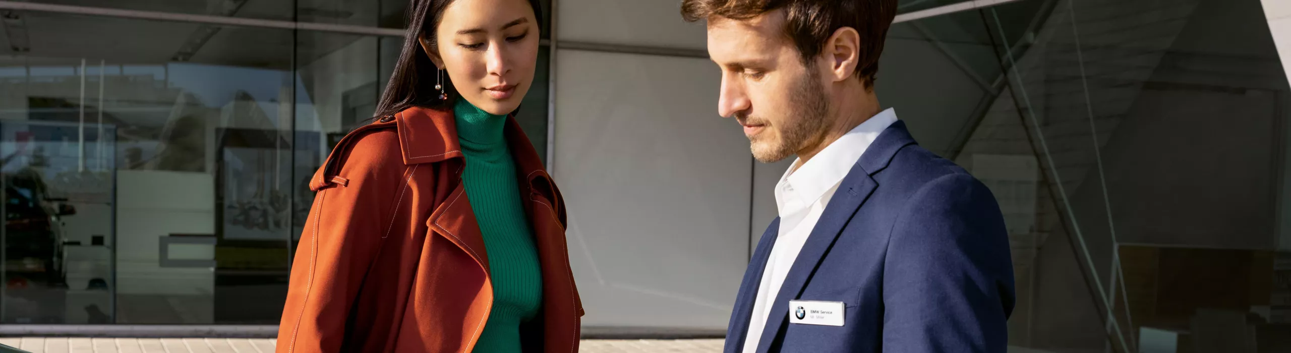 A person stands between a BMW saloon and a BMW SUV in front of an entrance area flanked by columns