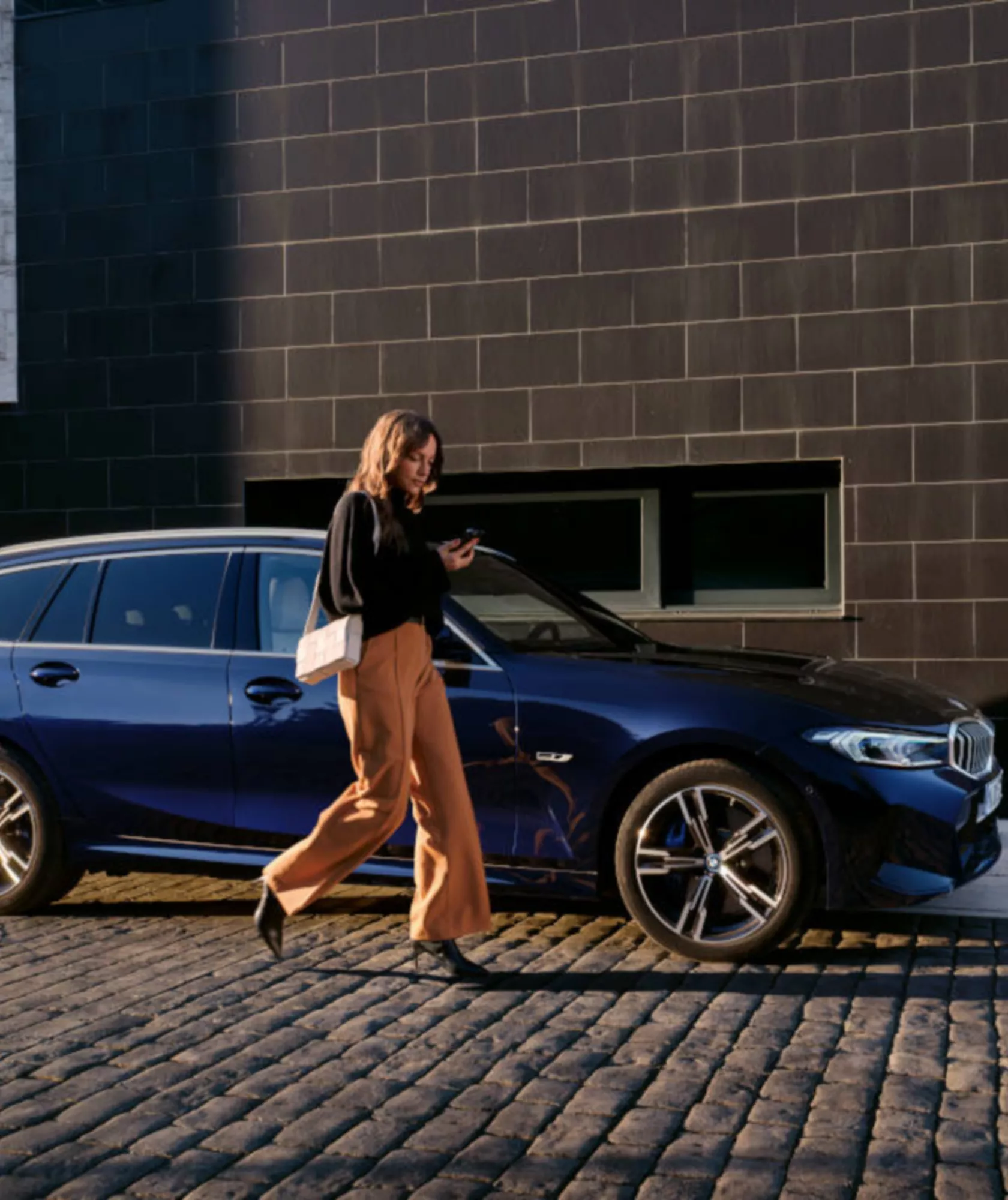 Person steht neben einem blauen BMW vor einem Gebäude.