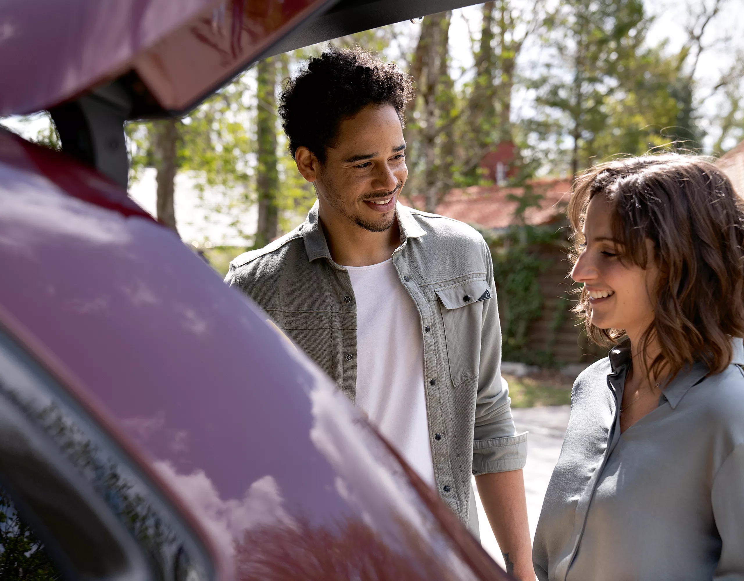 Un homme et une femme sourient devant le coffre ouvert d'une voiture rouge.