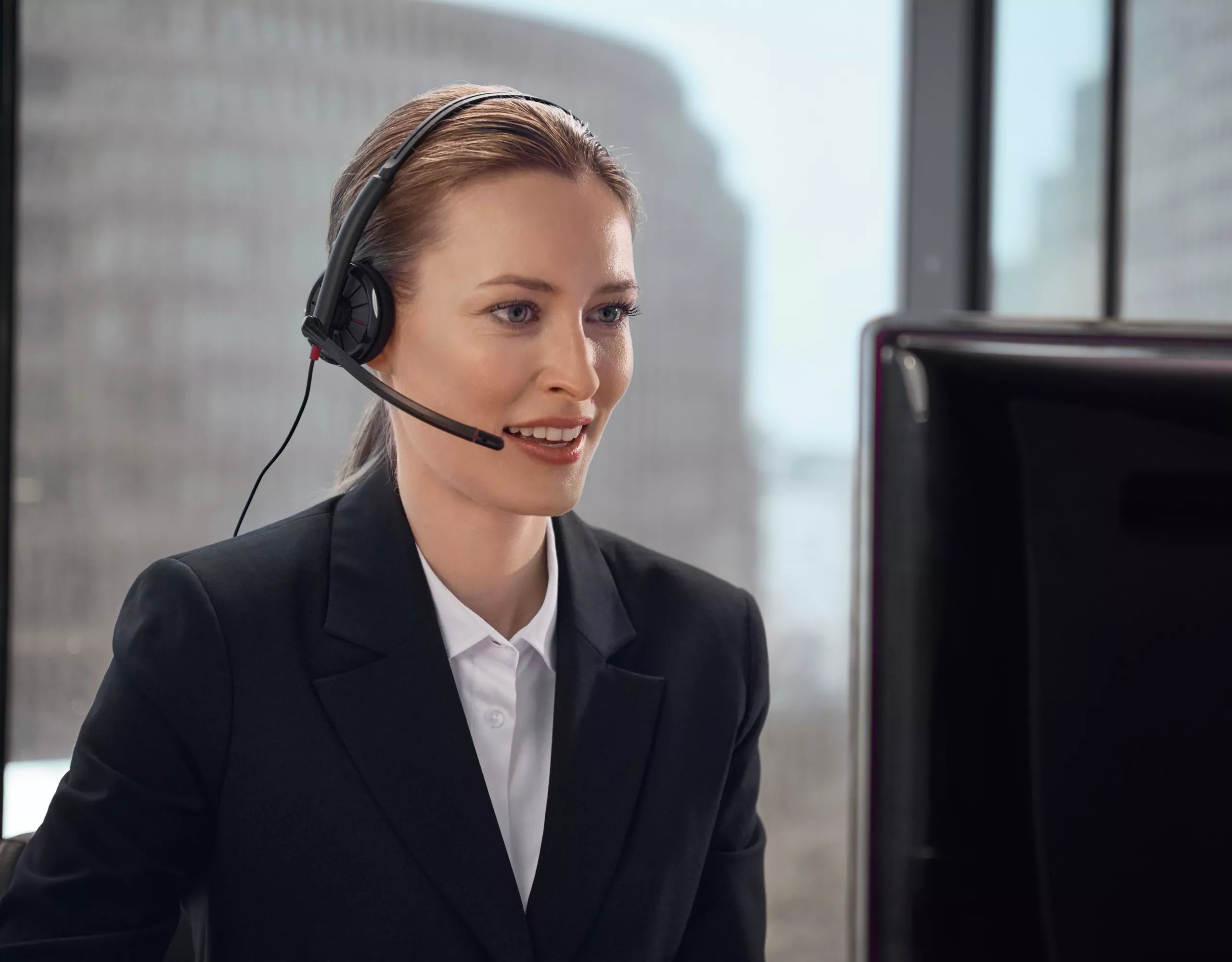 Person trägt ein Headset und sitzt vor einem Bildschirm.