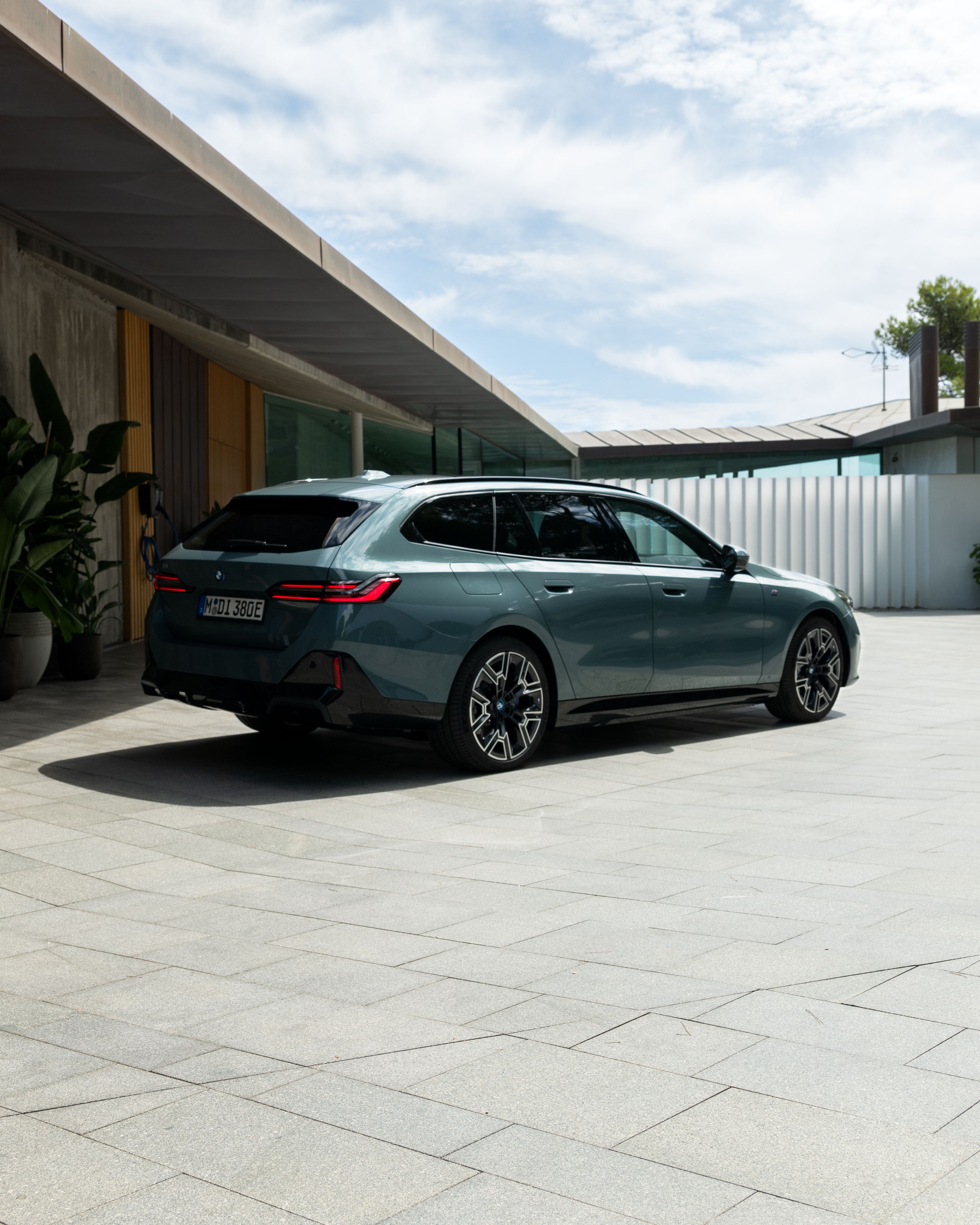 Ein grauer BMW Touring steht vor einem modernen Haus aus Beton und Holzelementen.