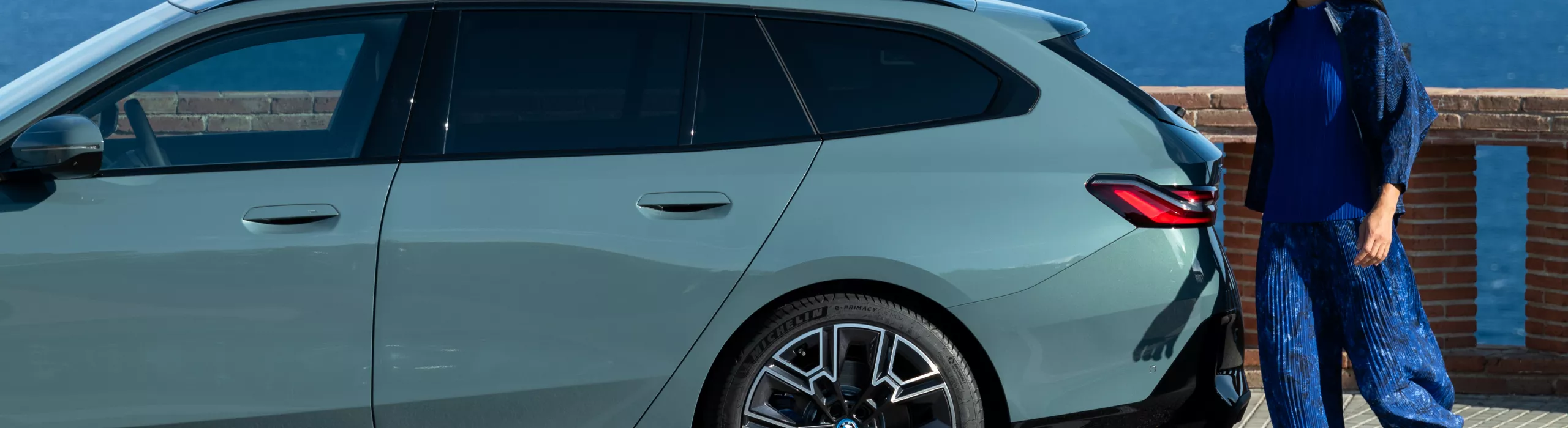 Eine Frau geht um das Hecks eines BMWs.