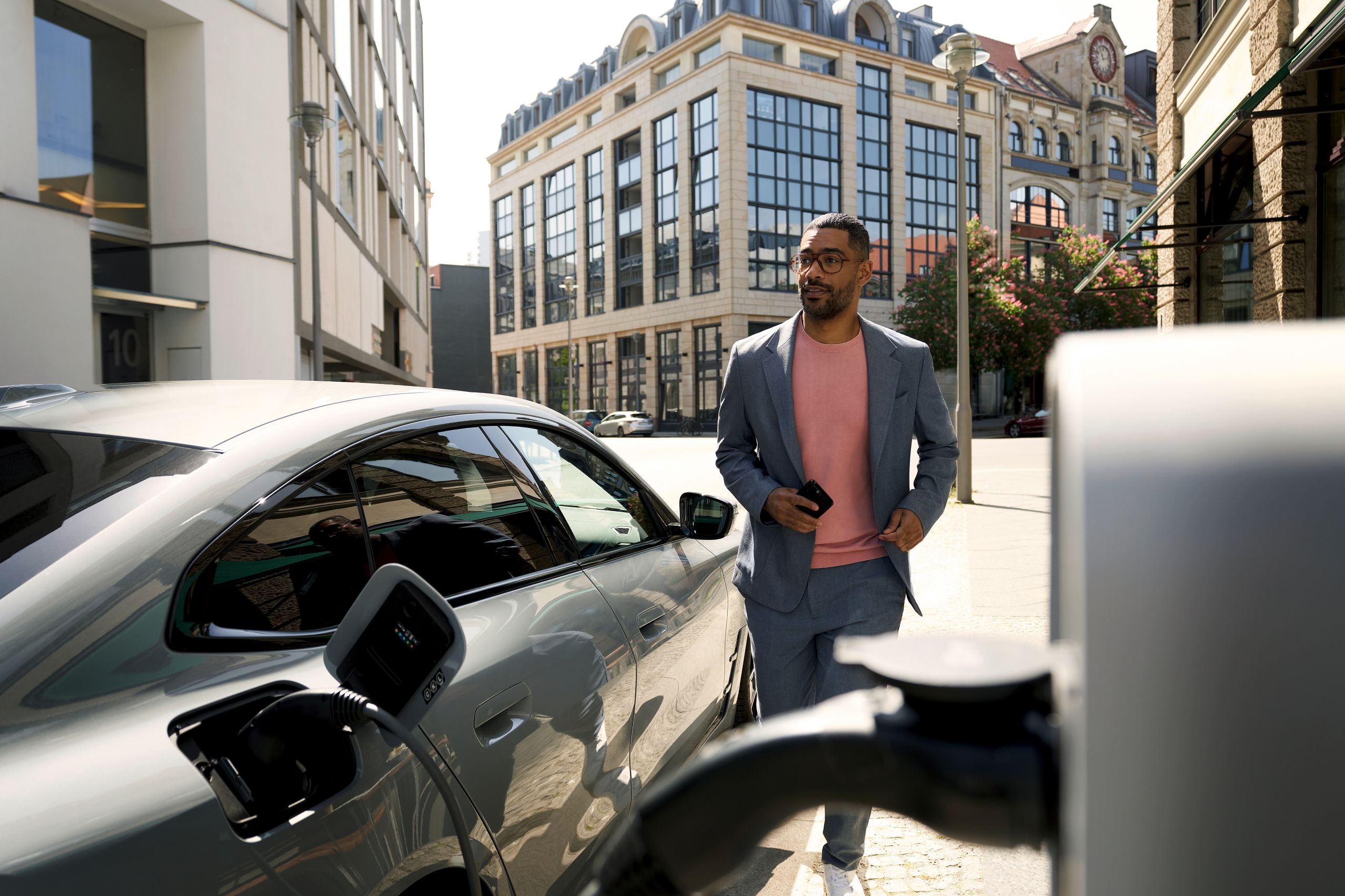 Man with phone in hand walking beside his BMW EV.