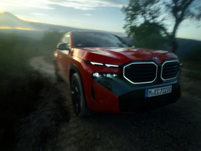 Ein roter sportlicher BMW fährt über eine Schotterstraße in einer grün bewachsenen Landschaft. 