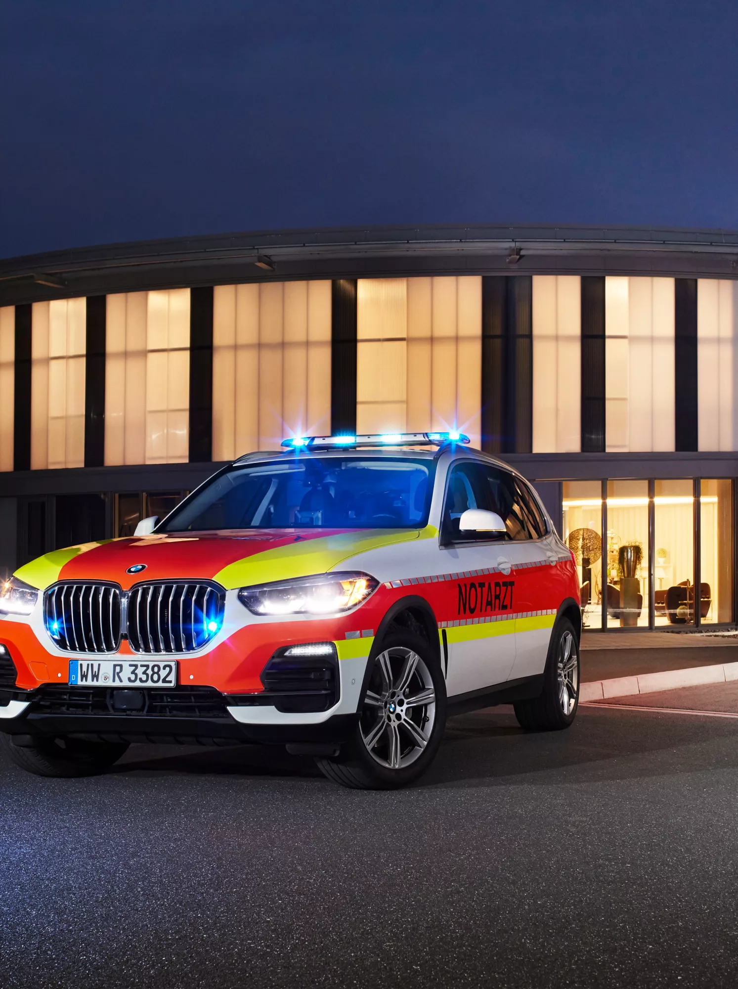 A BMW police vehicle drives past a lit-up building by twilight