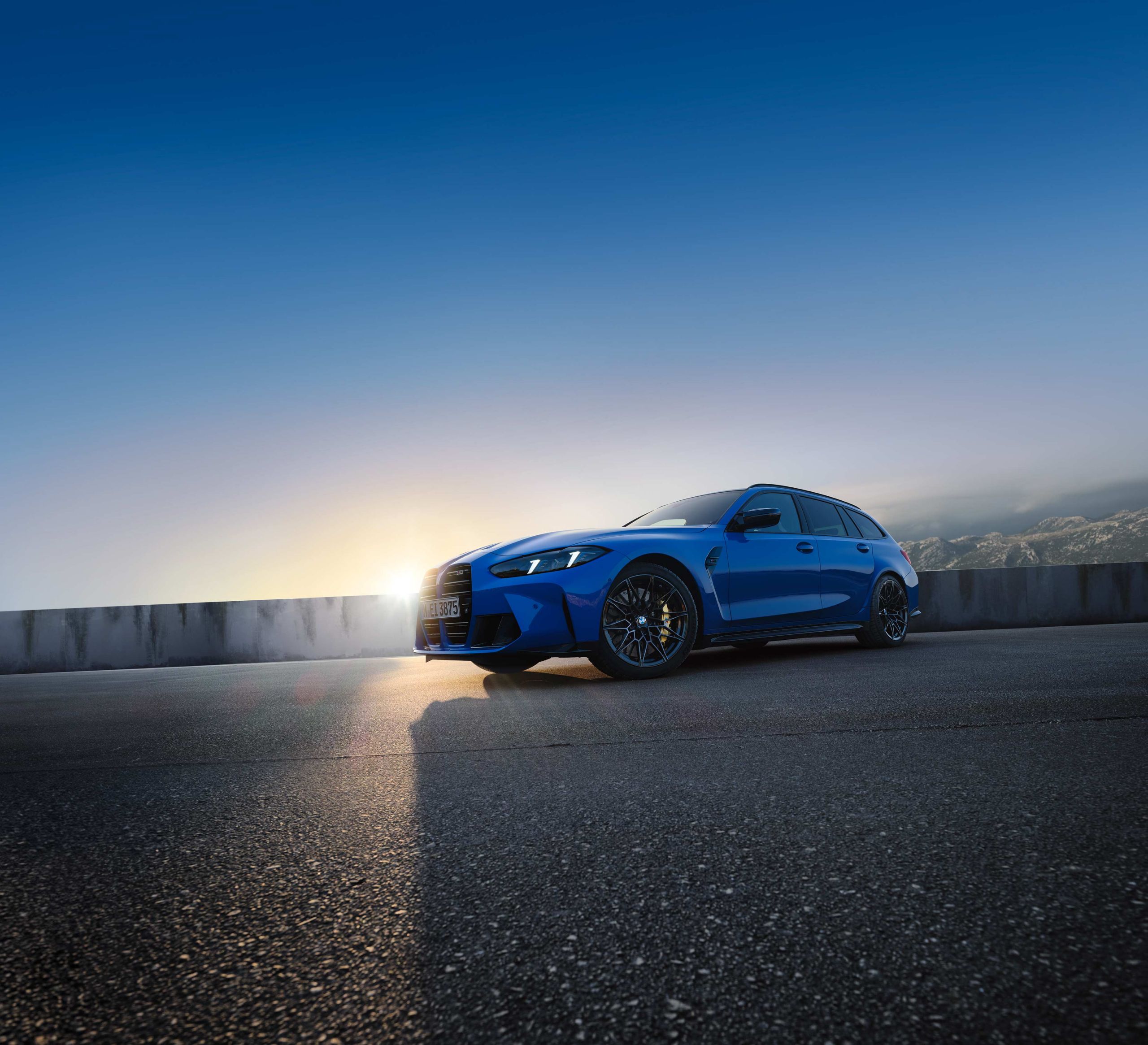BMW M3 Touring in blue parked at sunrise on a scenic mountain road with a dramatic sky