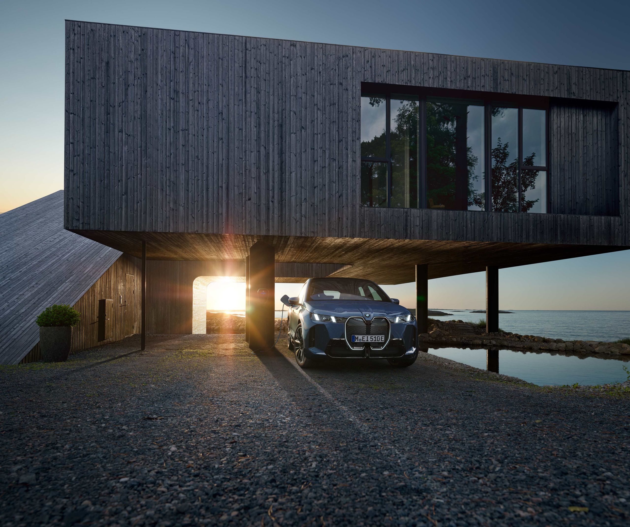 Ein BMW iX ist an einer Wallbox vor einem Haus vor einem See angeschlossen