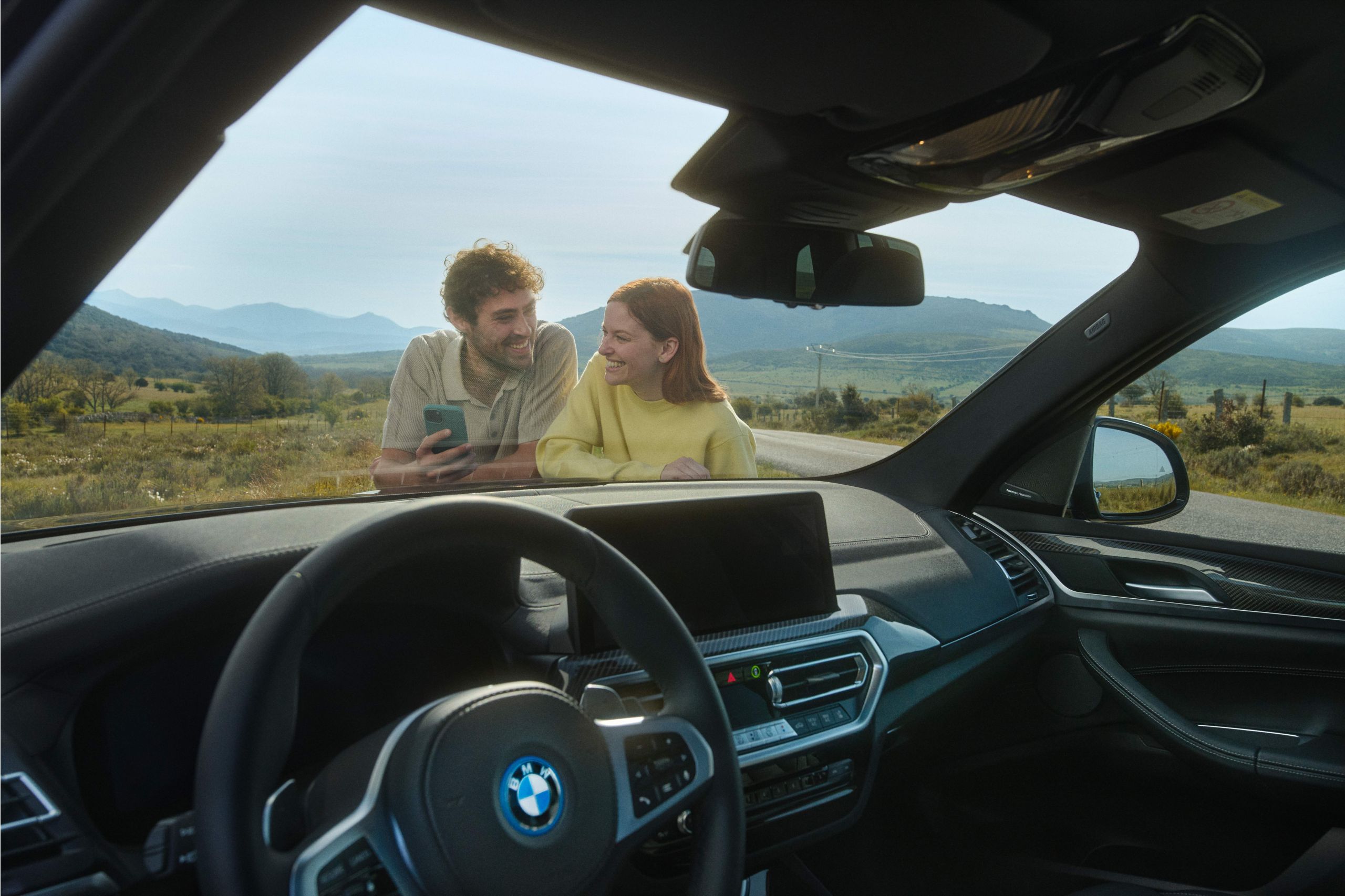 A fully electric BMW is plugged in to a charging station at the side of the road