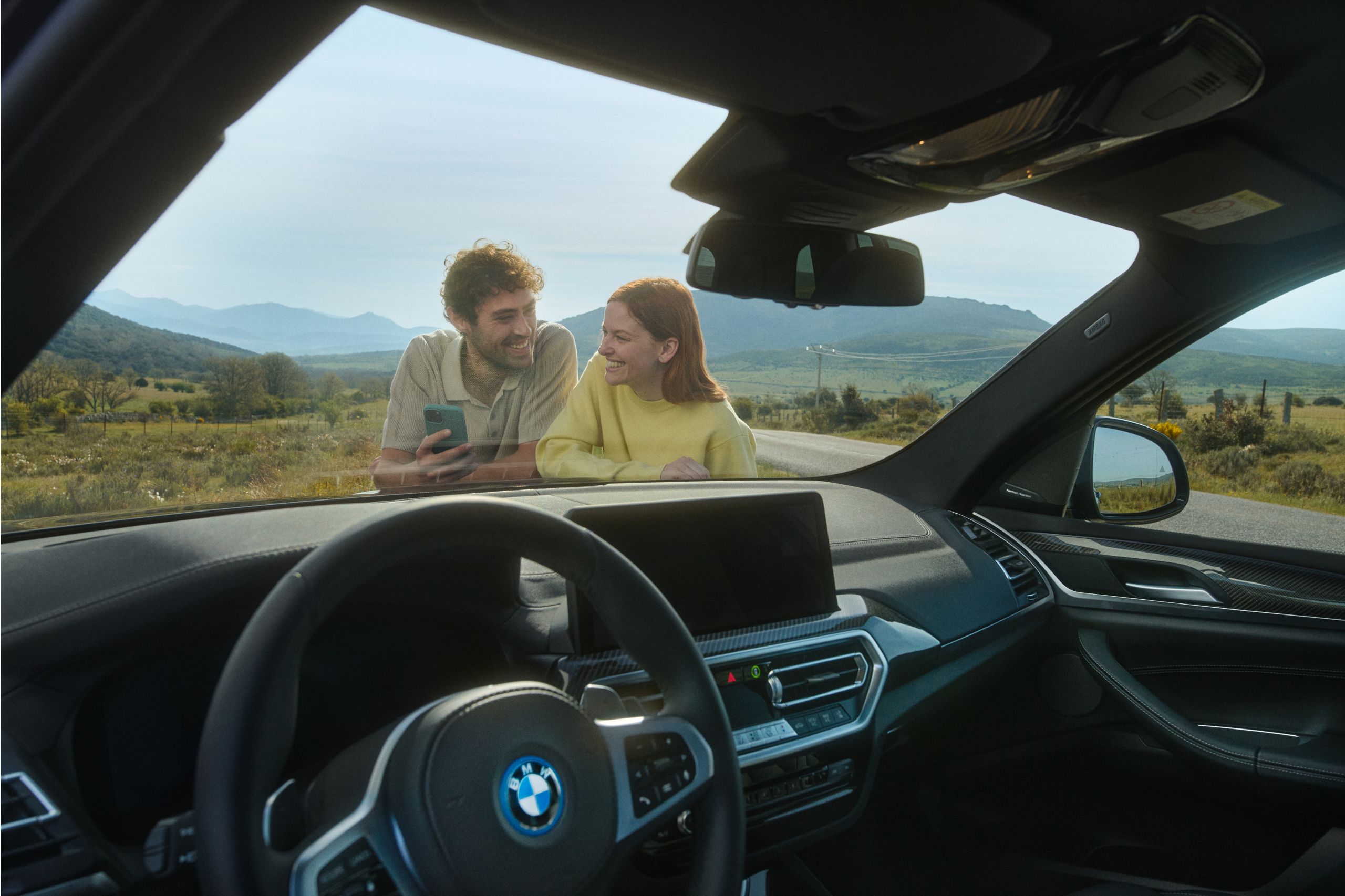 A fully electric BMW is plugged in to a charging station at the side of the road