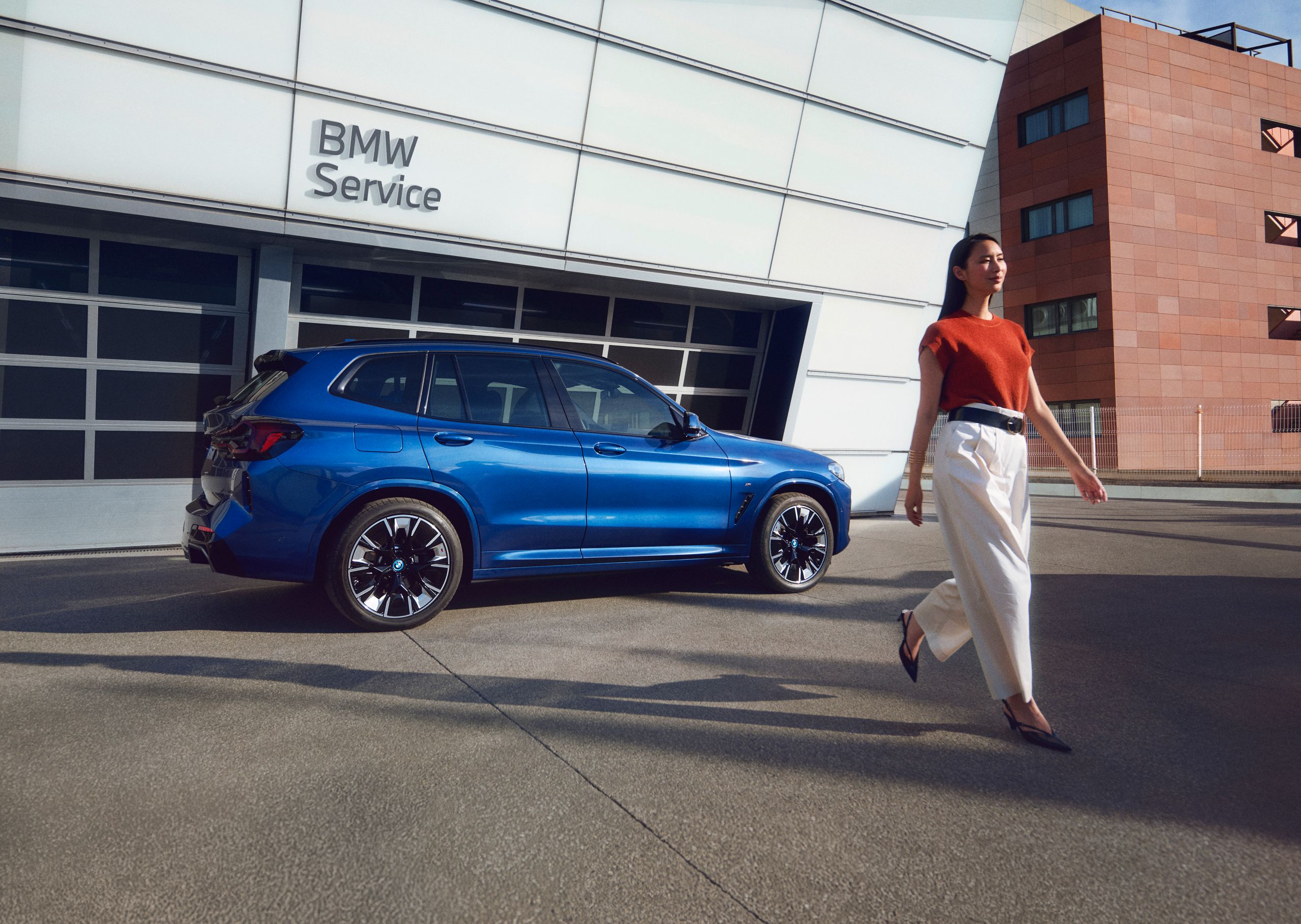 Ein blauer SUV von BMW steht vor den Garagentoren eines BMW Service Betriebs. Eine Frau geht von dem Fahrzeug weg.