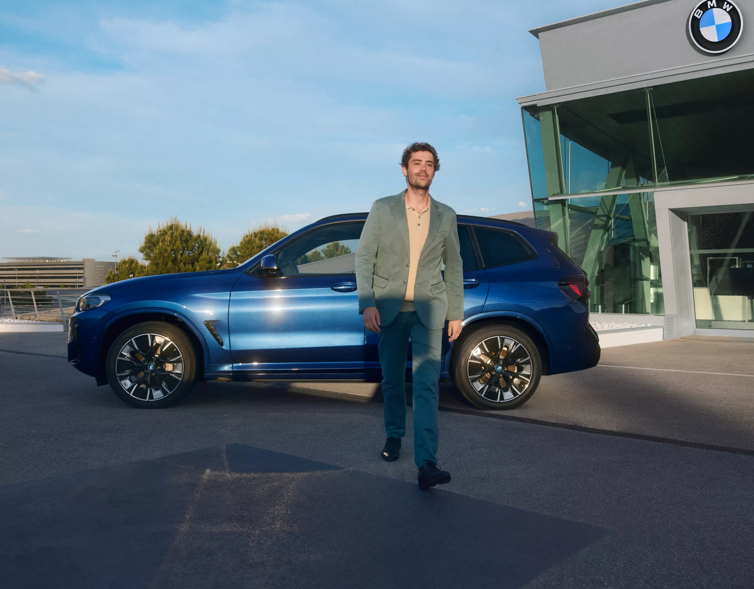 BMW Service Inclusive, egy töltőállomáson álló BMW i4 előtt egy férfi az okostelefonját nézi