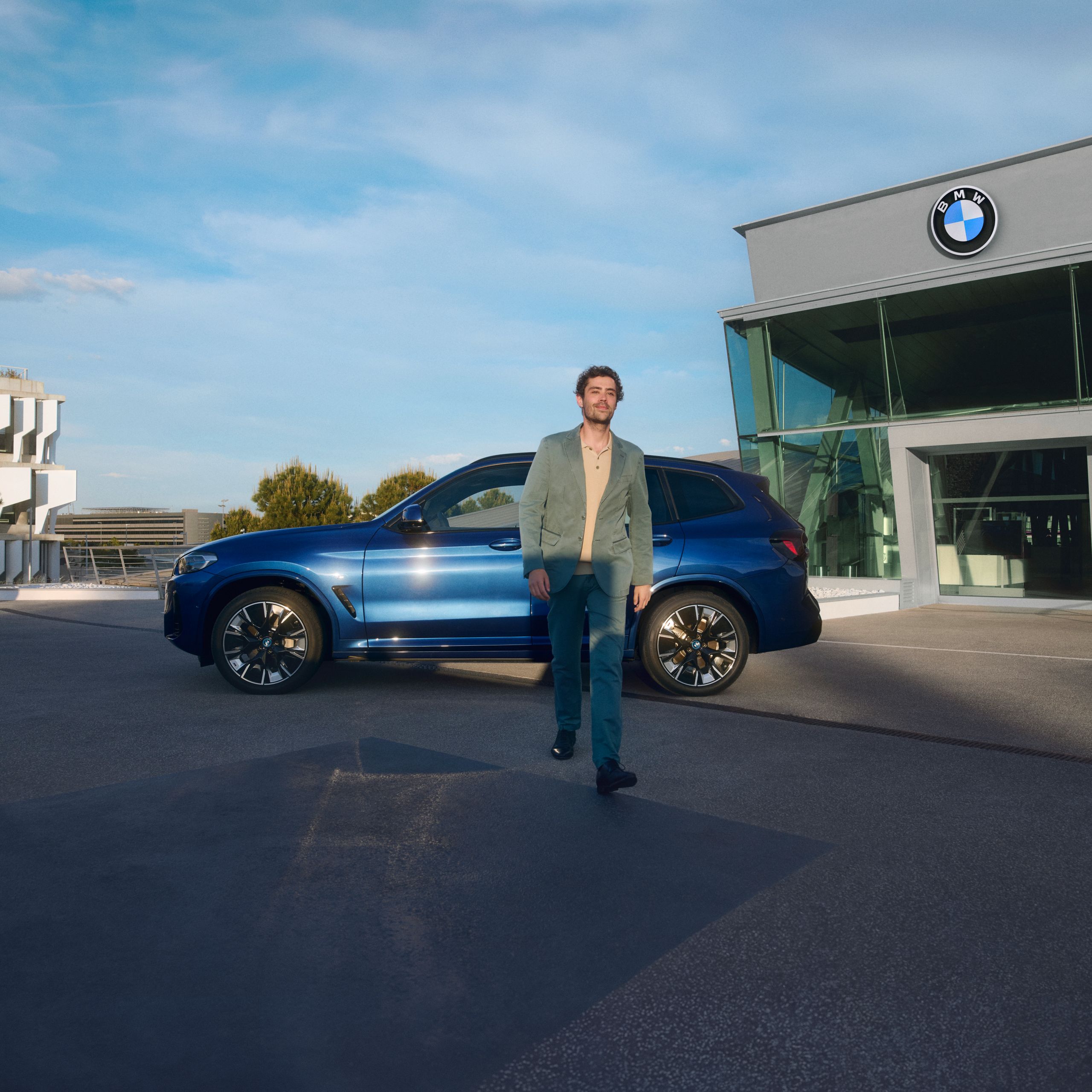 BMW Service Inclusive, egy töltőállomáson álló BMW i4 előtt egy férfi az okostelefonját nézi