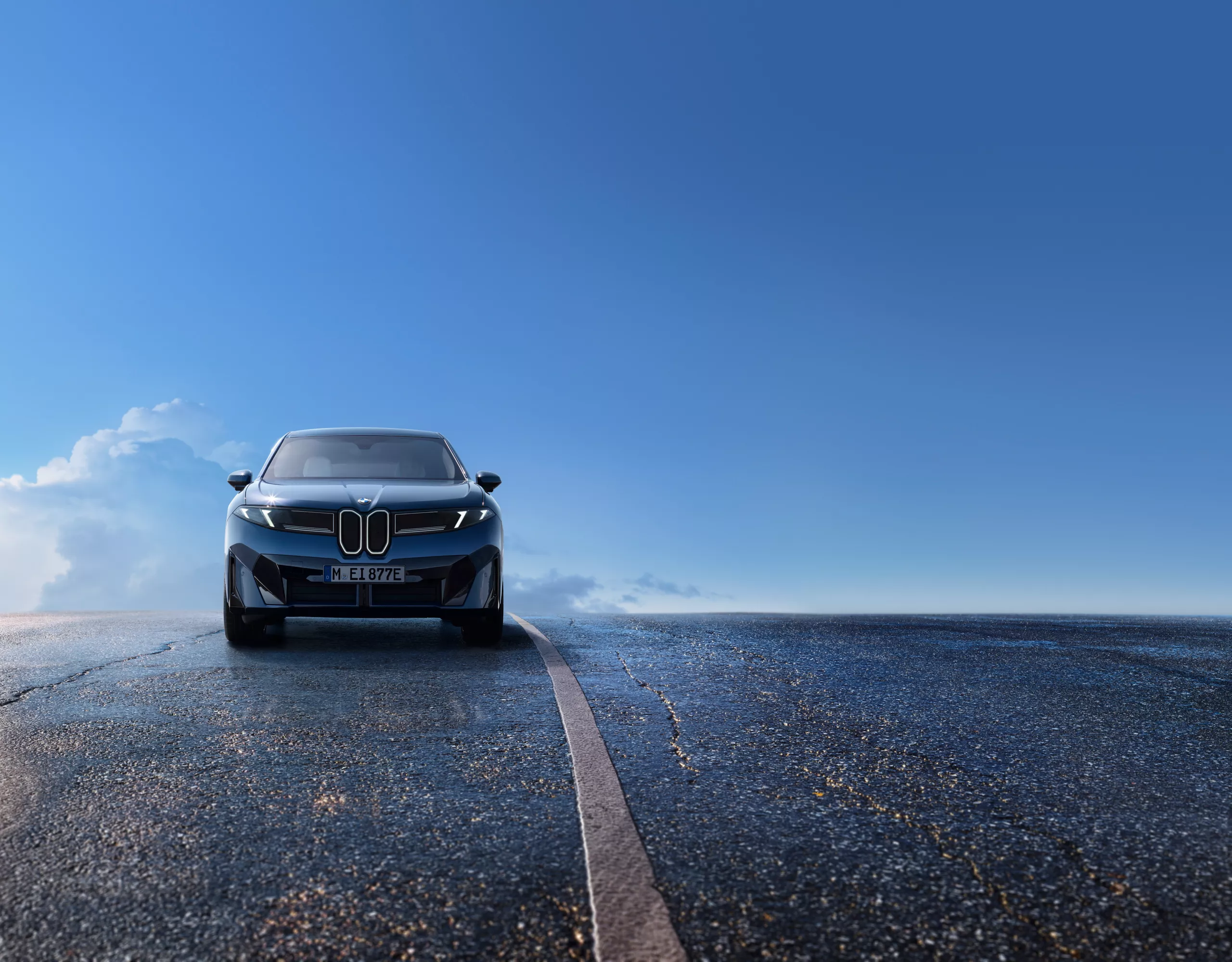 BMW iX3 frontal auf nasser Straße unter blauem Himmel, moderne LED-Scheinwerfer und markante Frontansicht