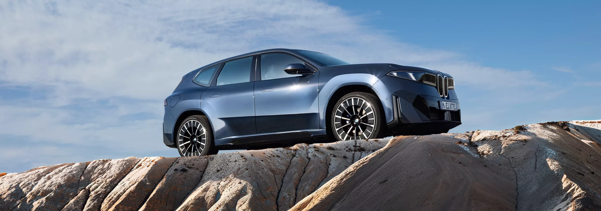 BMW iX3 steht auf felsigem Terrain unter klarem Himmel, Seitenansicht mit markanter Silhouette und großen Rädern