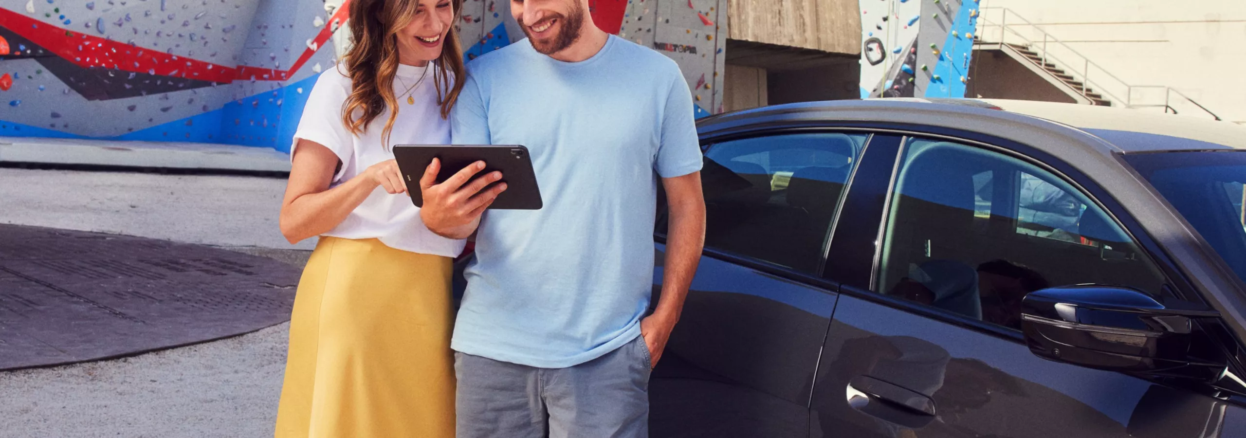 Un uomo e una donna sorridenti guardano un tablet davanti a una BMW i4