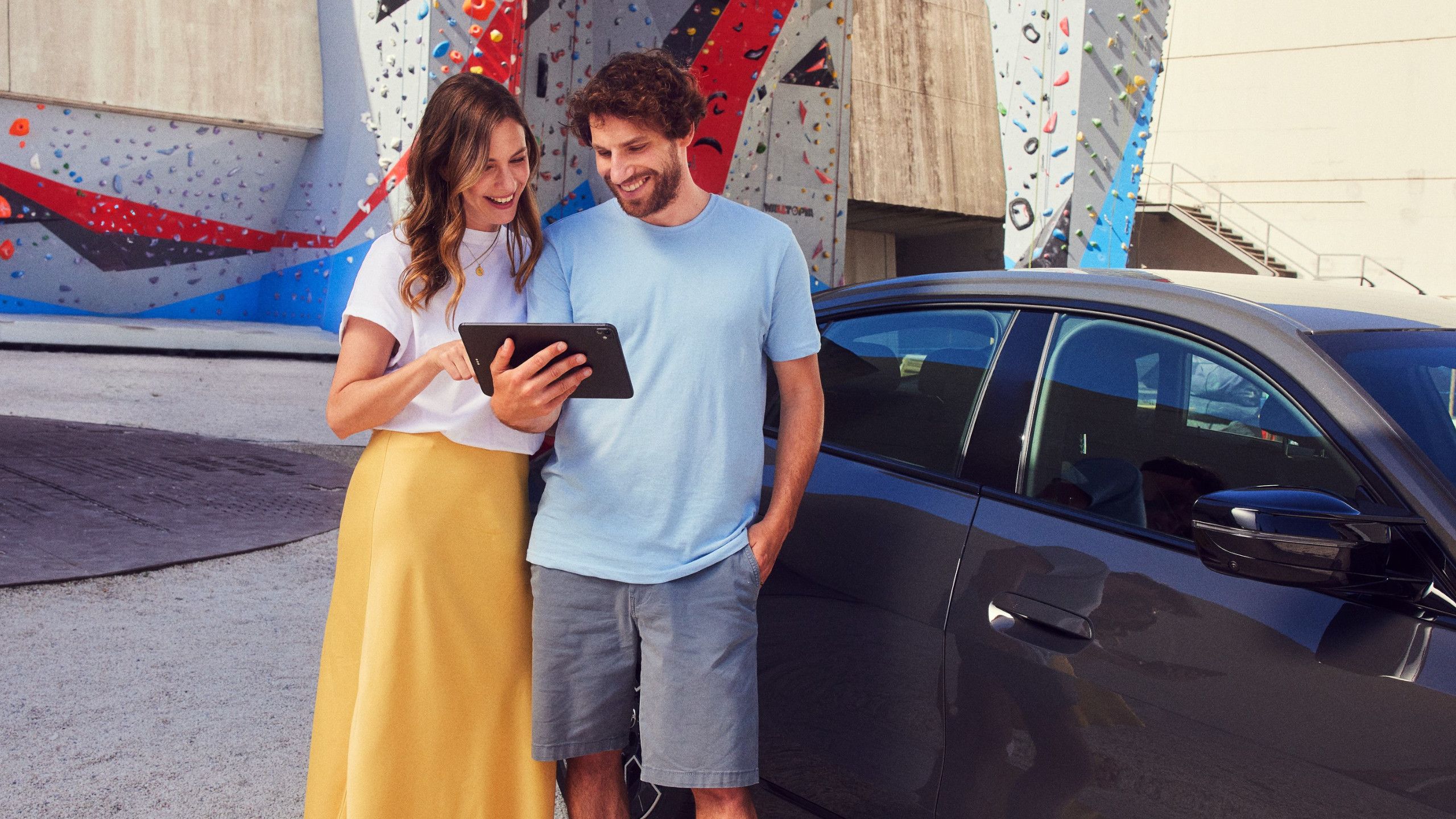 Un uomo e una donna sorridenti guardano un tablet davanti a una BMW i4