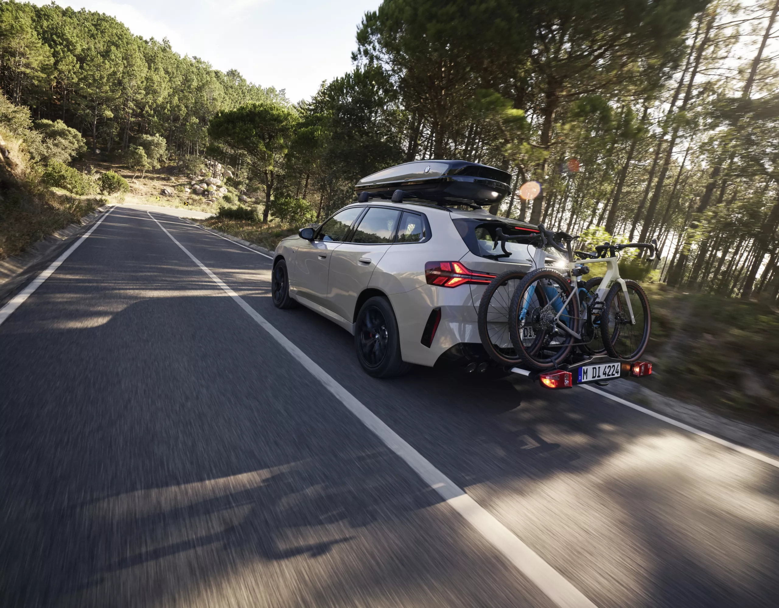 BMW X3 M50 xDrive equipado com suporte para bicicletas e caixa de tejadilho a circular na estrada.