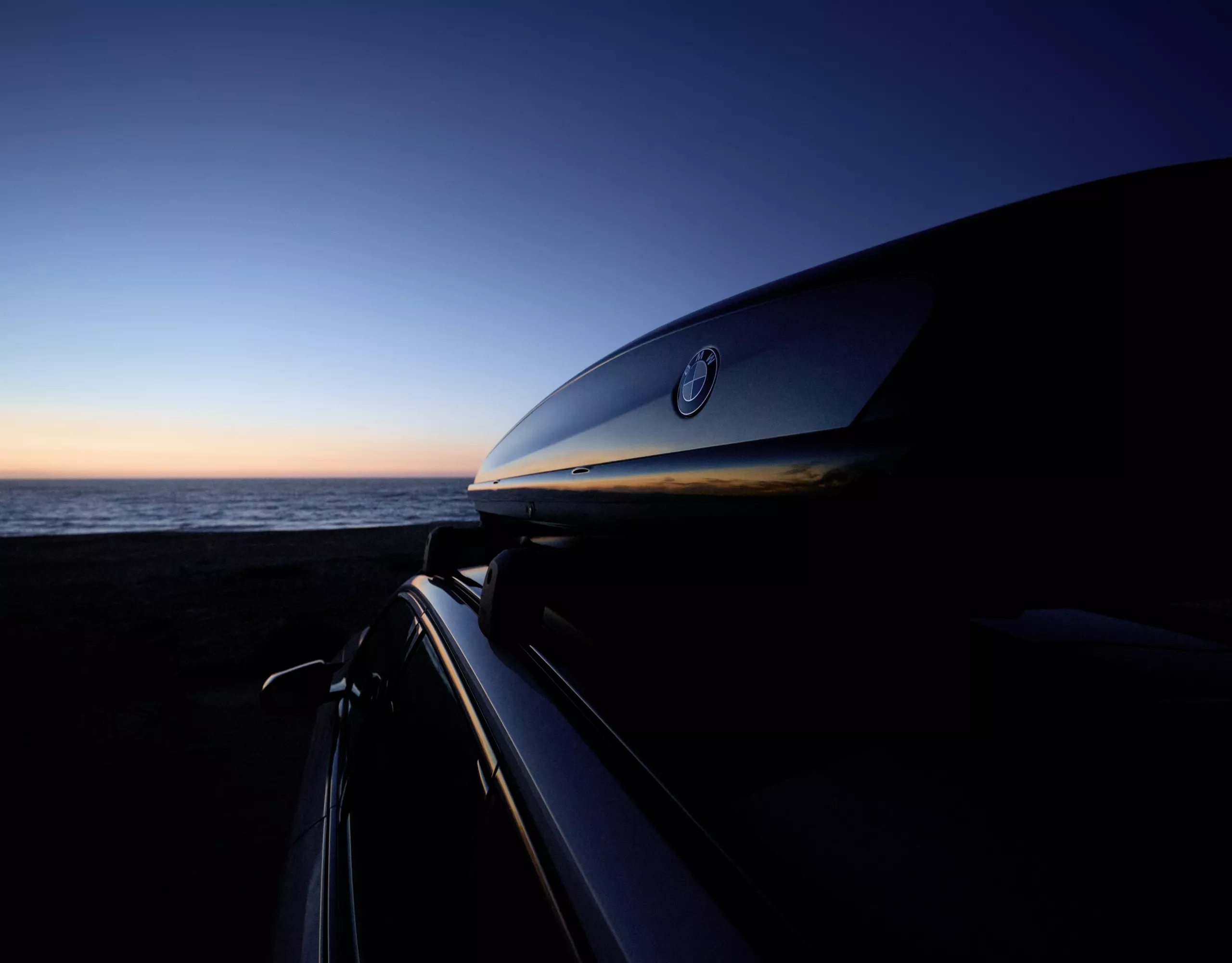 A woman and a man are standing in front of a BMW parked on an open field; the vehicle is equipped with Original BMW accessories
