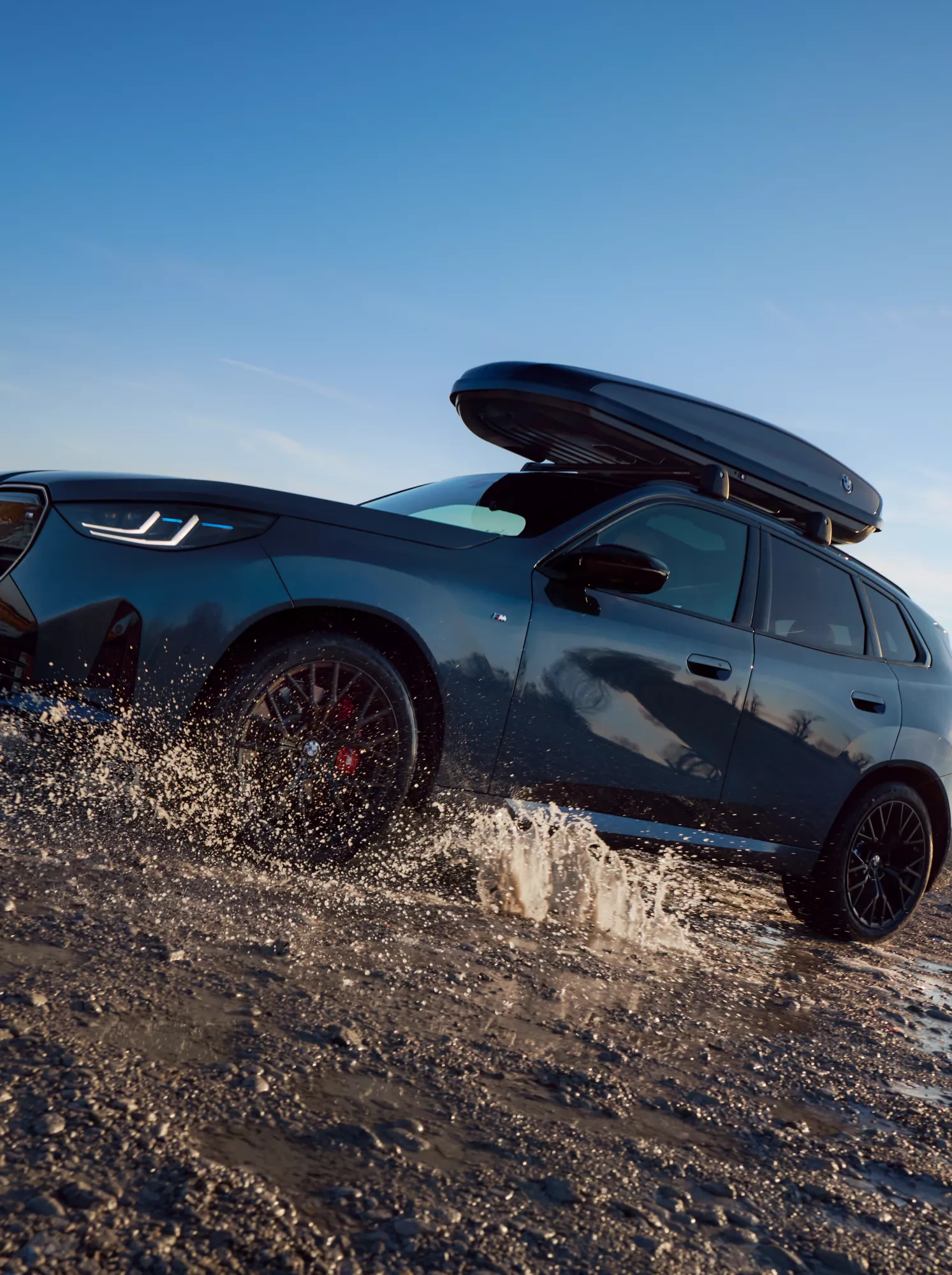 Een BMW iX1 en een BMW iX2 staan naast elkaar op een plateau bij zonsondergang