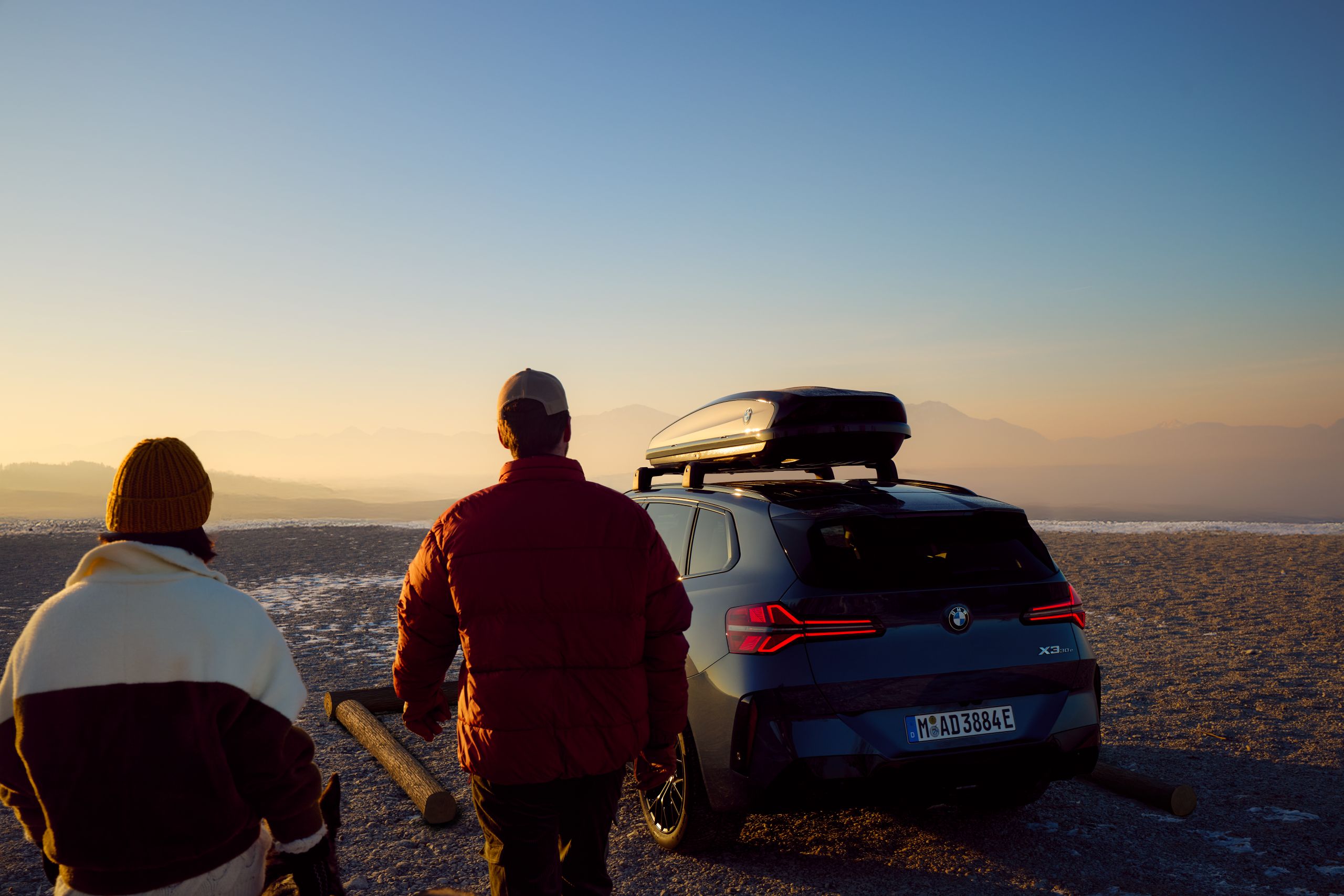Une personne se tient debout devant une BMW sur la plage