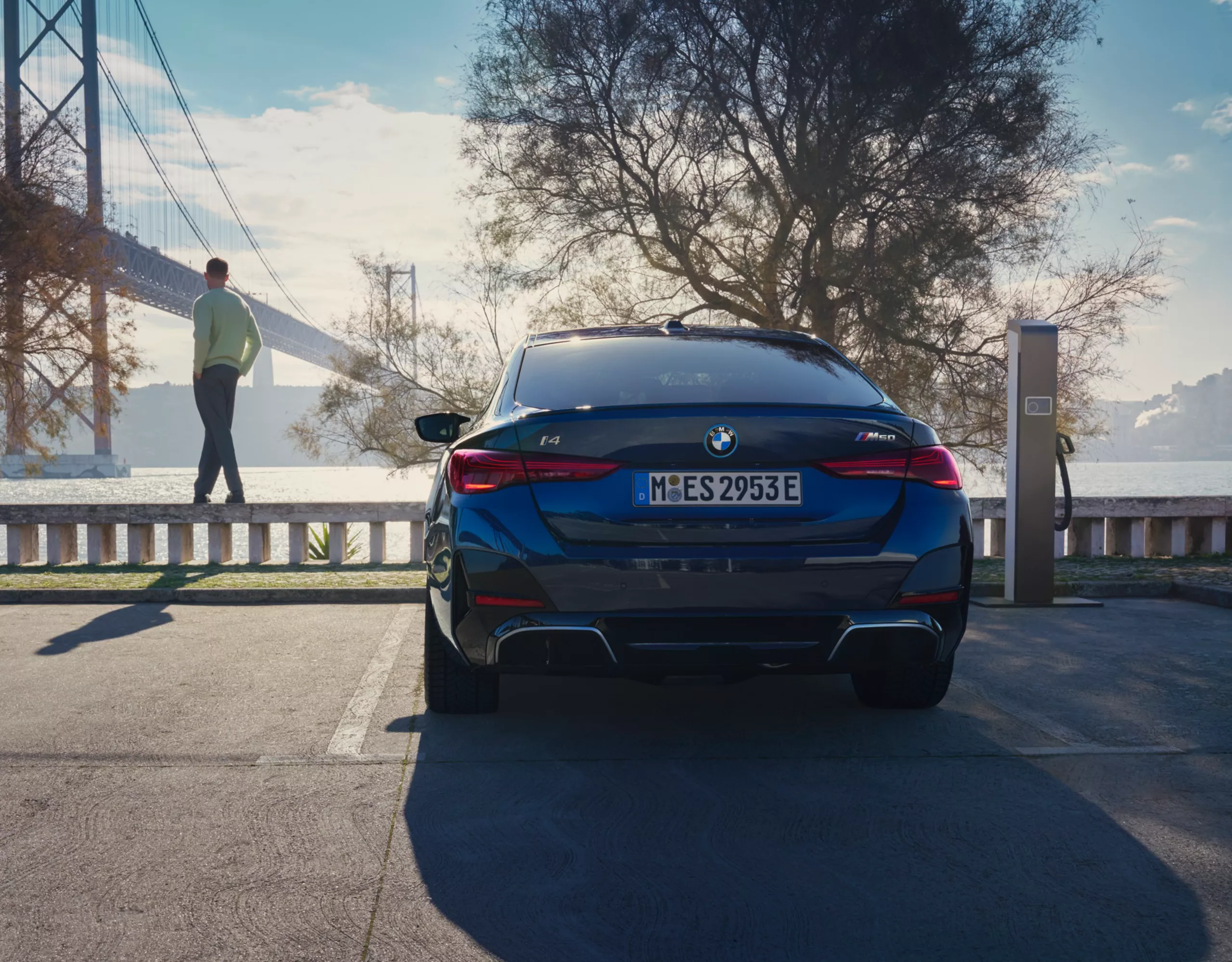 Un veicolo elettrico BMW grigio viene ricaricato. Accanto c’è una donna.