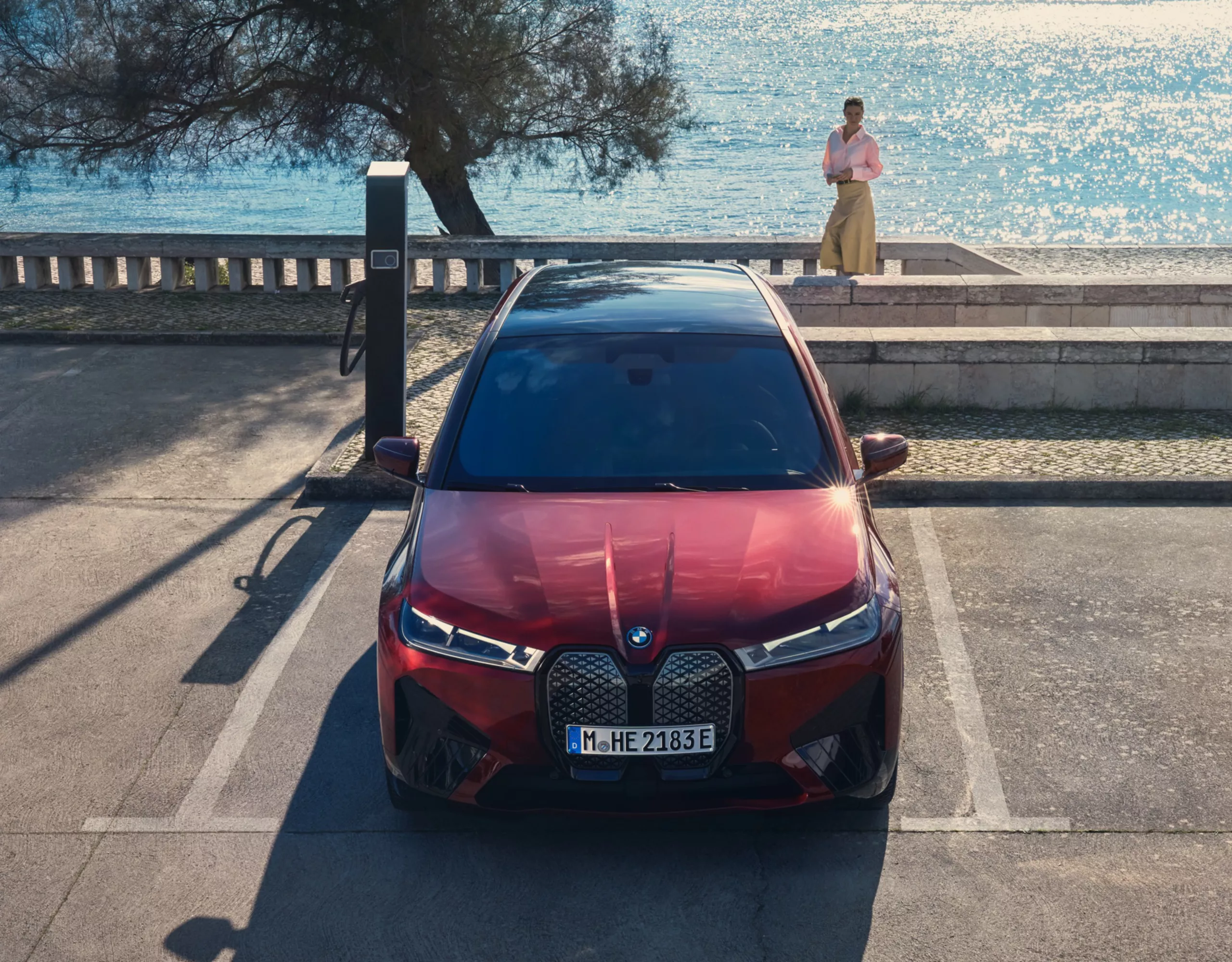 Vista frontale di una BMW nera. La BMW è accanto a una colonnina di ricarica.