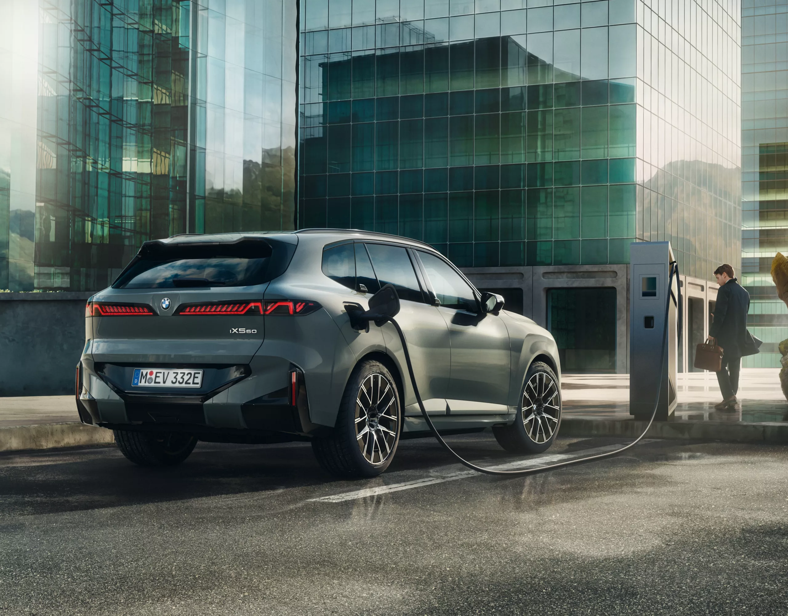 A BMW is parked in front of a charging station in front of a modern highrise