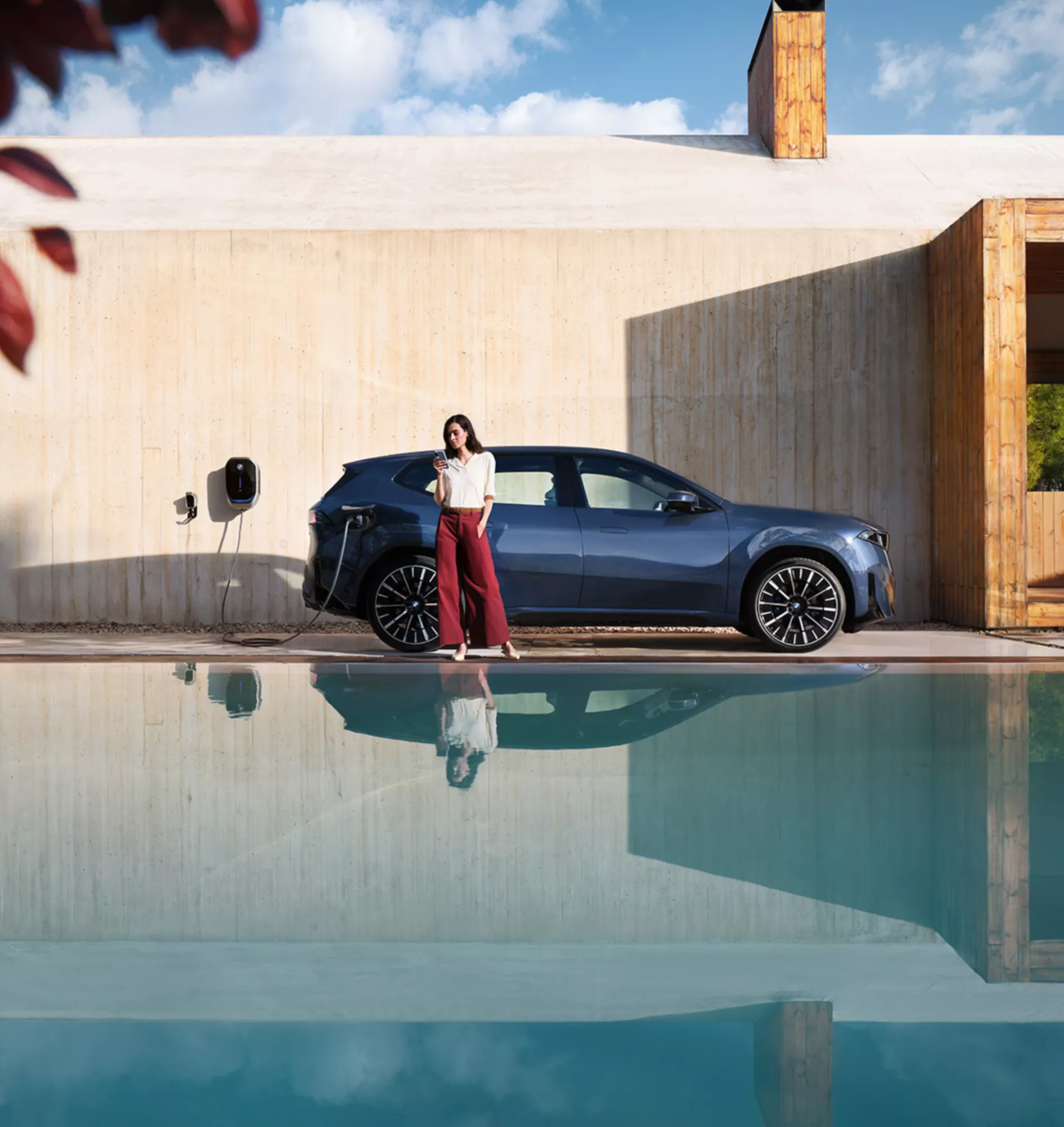 Une femme est assise dans une BMW, la porte ouverte. Un homme est appuyé contre la voiture, avec une maison en arrière-plan.